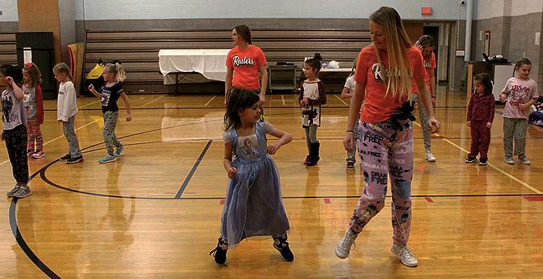 A cheerleader and her younger partner practice their dance moves.
