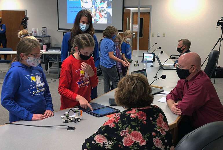 O'Loughlin fifth-graders Addy Day and Lauren Smith demonstrate their coding skills with a Lego robot to Hays school board members Tammy Wellbrock and Mike Walker as their teacher Gina Johnson looks on.