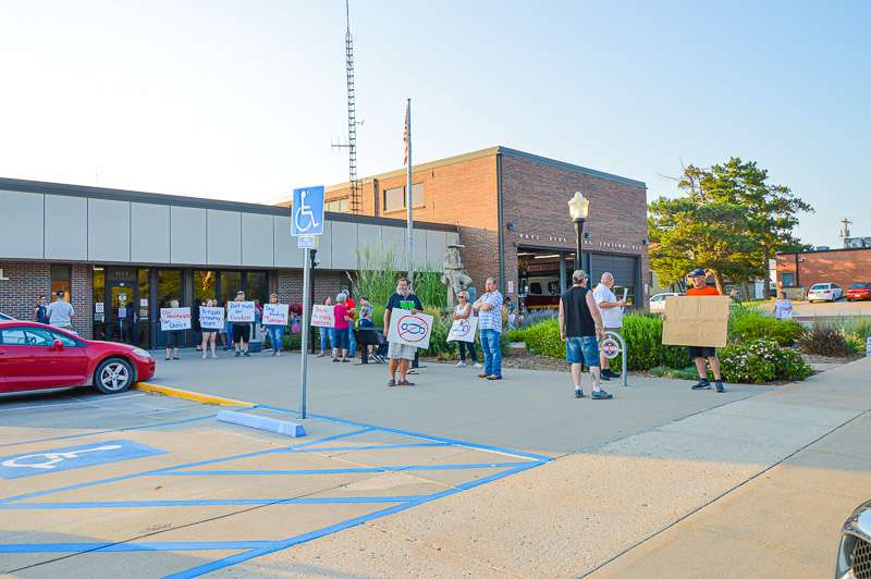 About 25 adults and children gather outside city hall protesting the face mask ordinance in Hays prior to Thursday's city commission meeting. (Photo by James Bell/Hays Post)