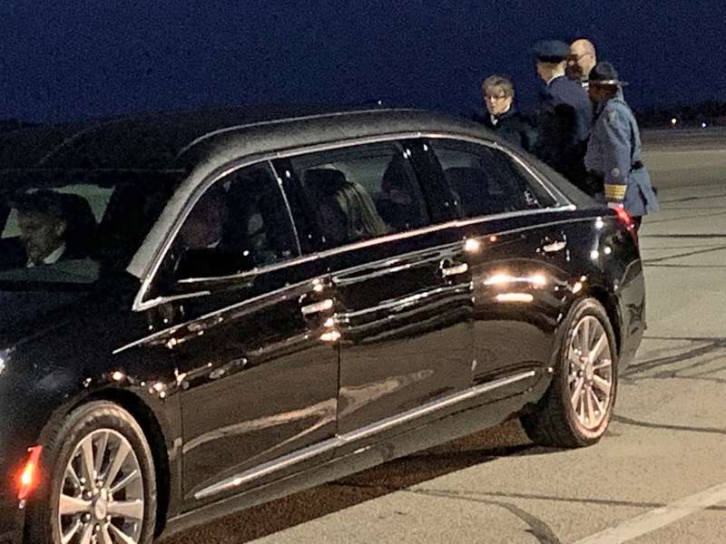 <b>Kansas Governor Laura Kelly and other dignitaries stand behind the Dole family limousine.</b>
