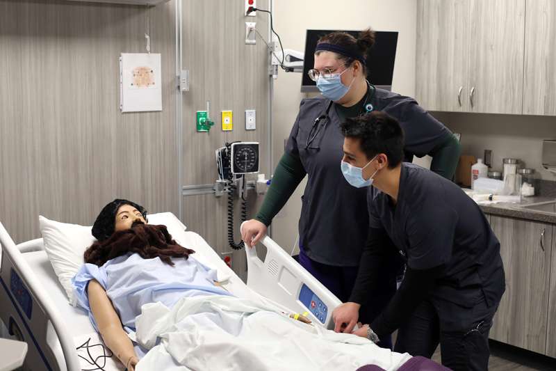 <b>Ethan Asur, right, talks to the patient in the simulation lab at Kansas Wesleyan University on Jan. 12, 2021. He and classmate Sara Taylor, left, were participating in a simulation to help students learn how to treat a diabetic patient with a low blood sugar. The newly opened Nursing Education Center at KWU houses two simulation suites and also a skills lab.</b> Photo by Karen Bonar courtesy KWU