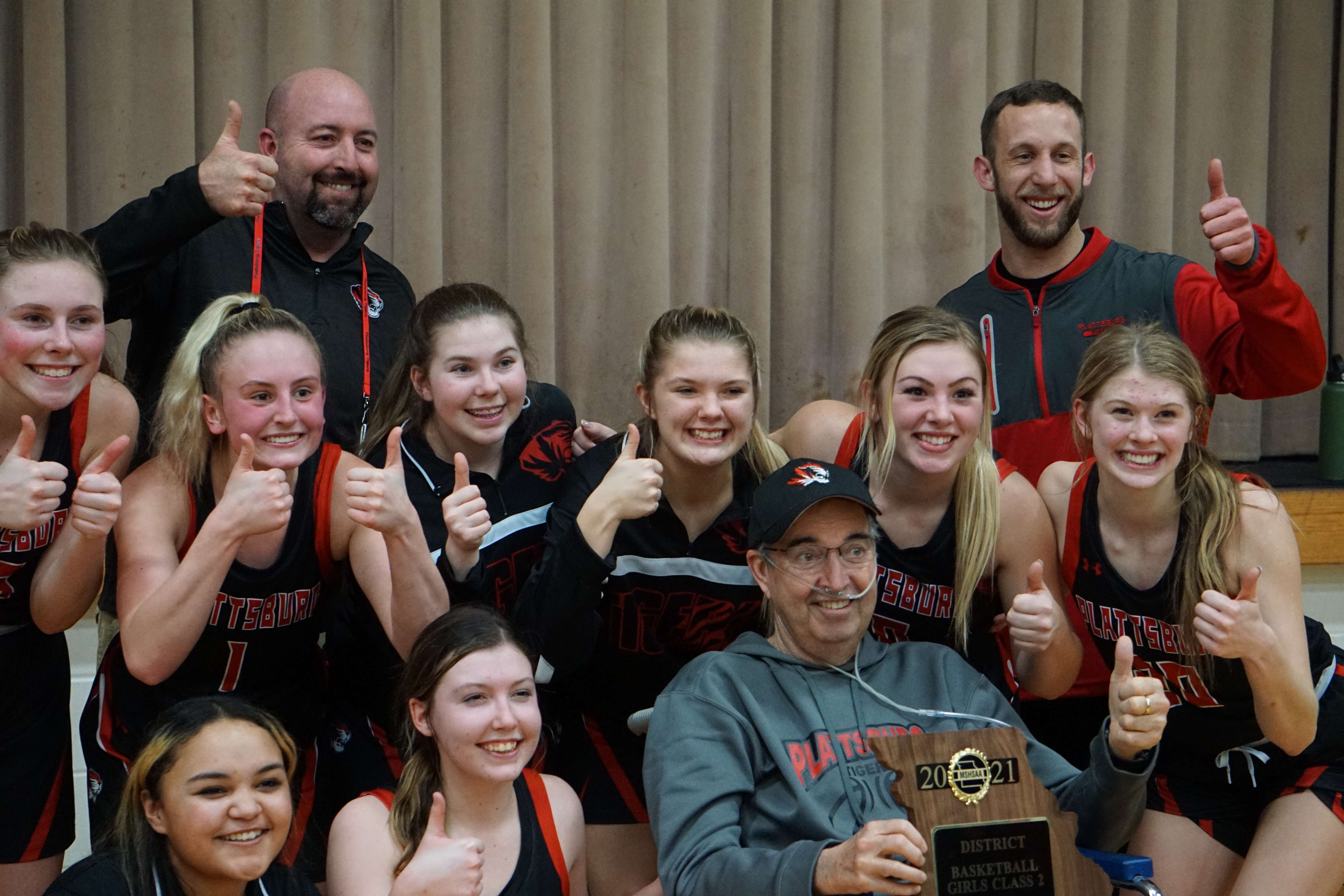 Plattsburg girls' basketball coach Chris Hodge (back row, top left) celebrates with his team and his father, Randy (bottom, center right) after the Tigers' win over Mid-Buchanan in the Class 2 District 15 title game Friday. Photo by Tommy Rezac.