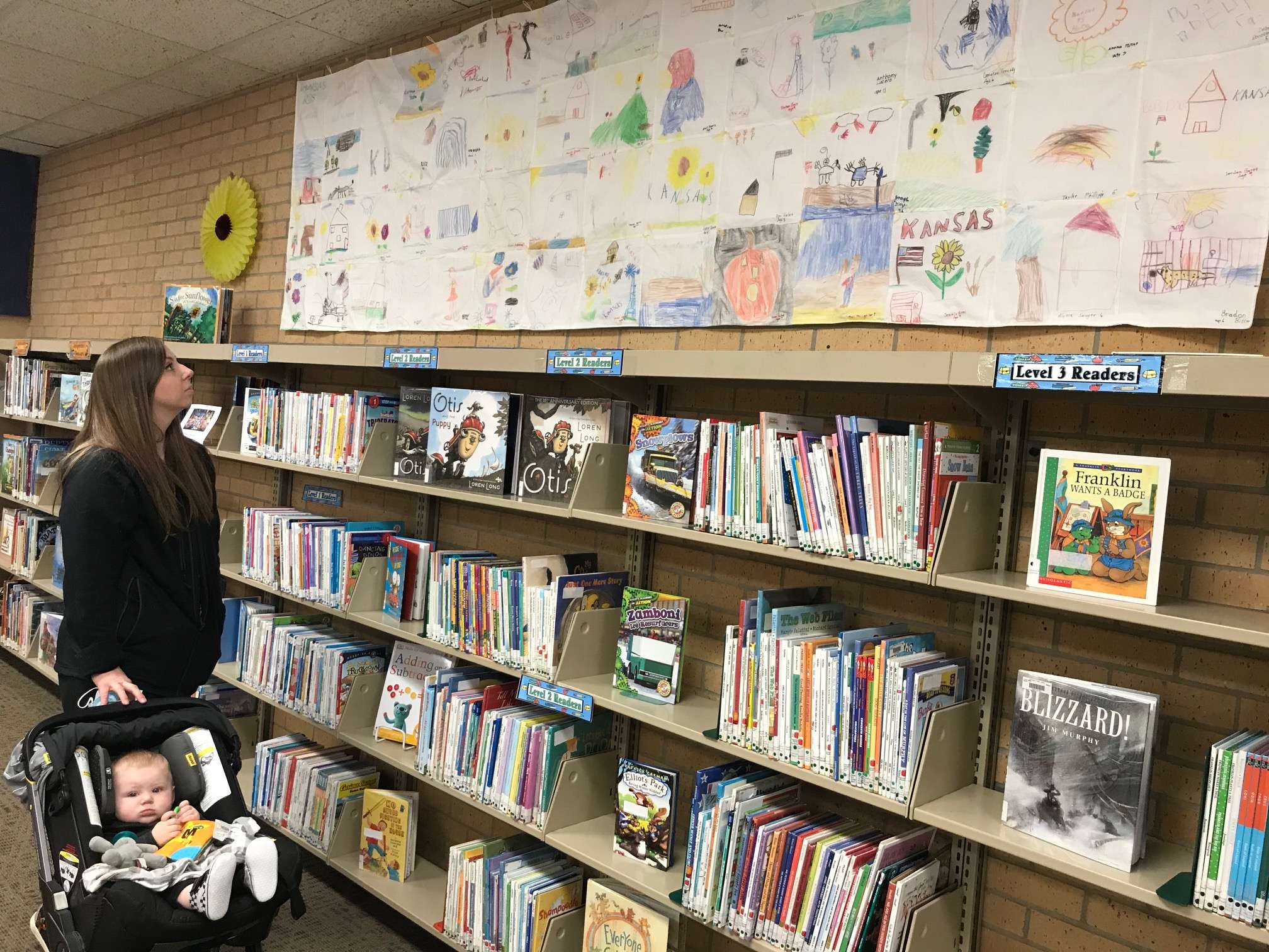 Sarah (Ritter) Smith and eight-month-old son Archer, take a look at the Kansas quilt made by participants of Summer Reading at Hoisington Public Library in 1996.