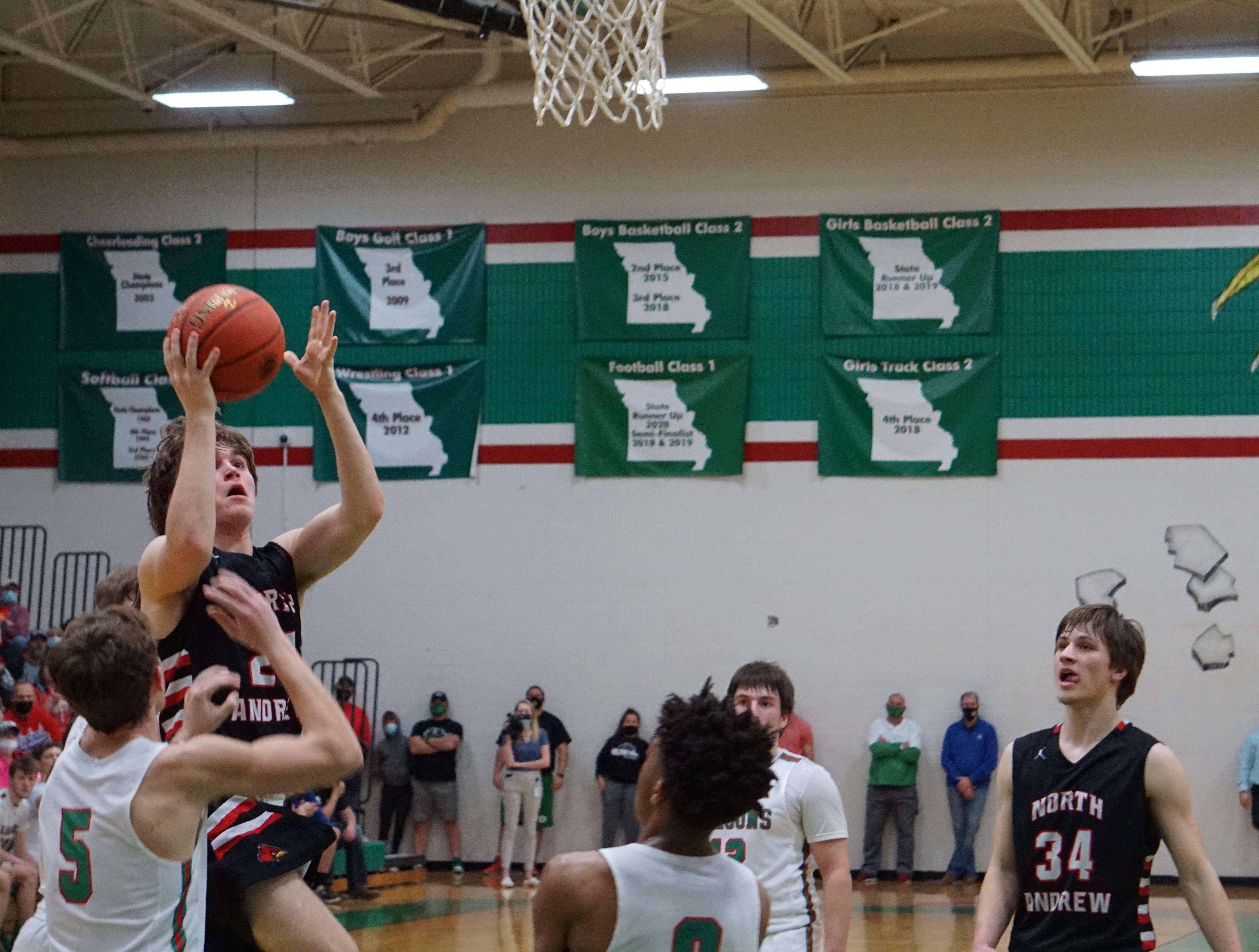 North Andrew's Hayden Ecker (left) goes in for a layup against Mid-Buchanan's Blake Hunter (5) in the second half of the Cardinals' 48-45 win over the Dragons Tuesday. Photo by Tommy Rezac.
