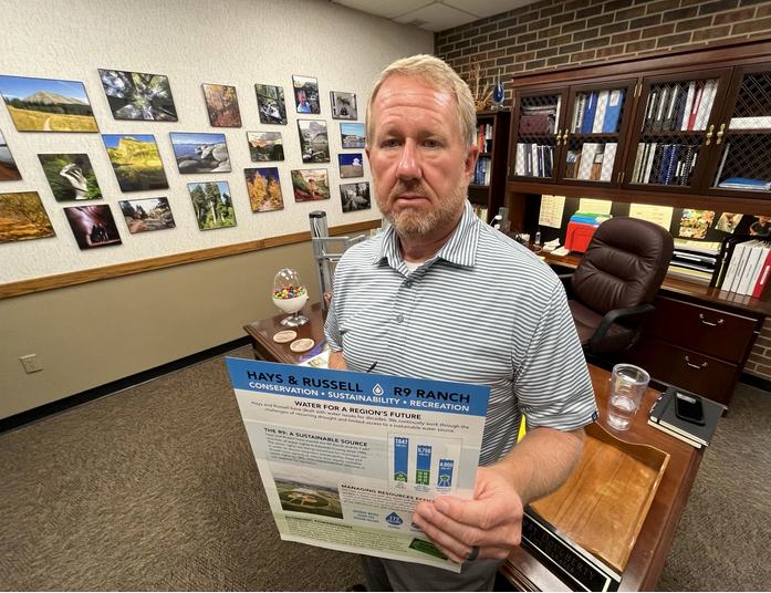 Toby Dougherty, Hays city manager, stands in his office holding a pamphlet that lays out the city's case for building a water pipeline to its R9 Ranch property in Edwards County. David Condos / Kansas News Service