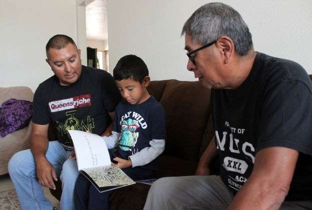 Micca Madalena, center, reads to his father, Darryl Madalena, left, and grandfather Myron Ami in his native language of Towa after getting home from school at Jemez Pueblo, N.M., Oct. 7, 2022. Darryl Madalena is advocating for more Native Americans to consider joining the organ donation rolls. (AP Photo/Susan Montoya Bryan)