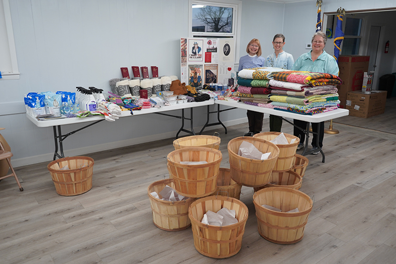 Natoma American Legion Auxiliary members (L-R), Laah Tucker, Linda Crawford, and Sharon MacConnell, packed bushel baskets filled with essential items and handmade quilts by St. John Lutheran Quilting Guild, Russell, for displaced women following the Four County Wildfires.