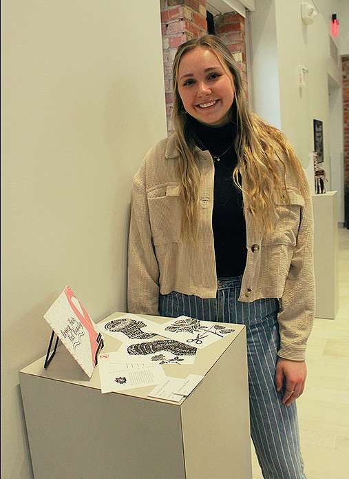Riley Tinder, a sophomore in graphic design from Basehor, with her postcards titled "Losing Hair, Not Beauty." Photo by Cristina Janney/Hays Post