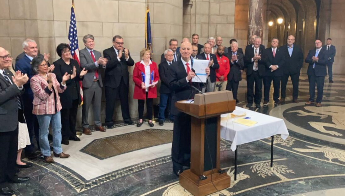Gov. Pete Ricketts holds up a copy of LB 873, the massive tax cut package, after he signed it into law on Wednesday. (Paul Hammel/Nebraska Examiner)