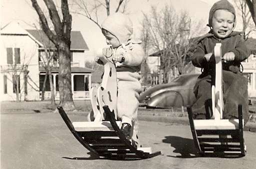 Toddlers Jack and Patty Russell play on their rocking horses in front of their grandfather, R. C. “Coe” Russell’s home on Broadway about 1940.  The home of Ezekiel and Anna McBride is pictured in the background.