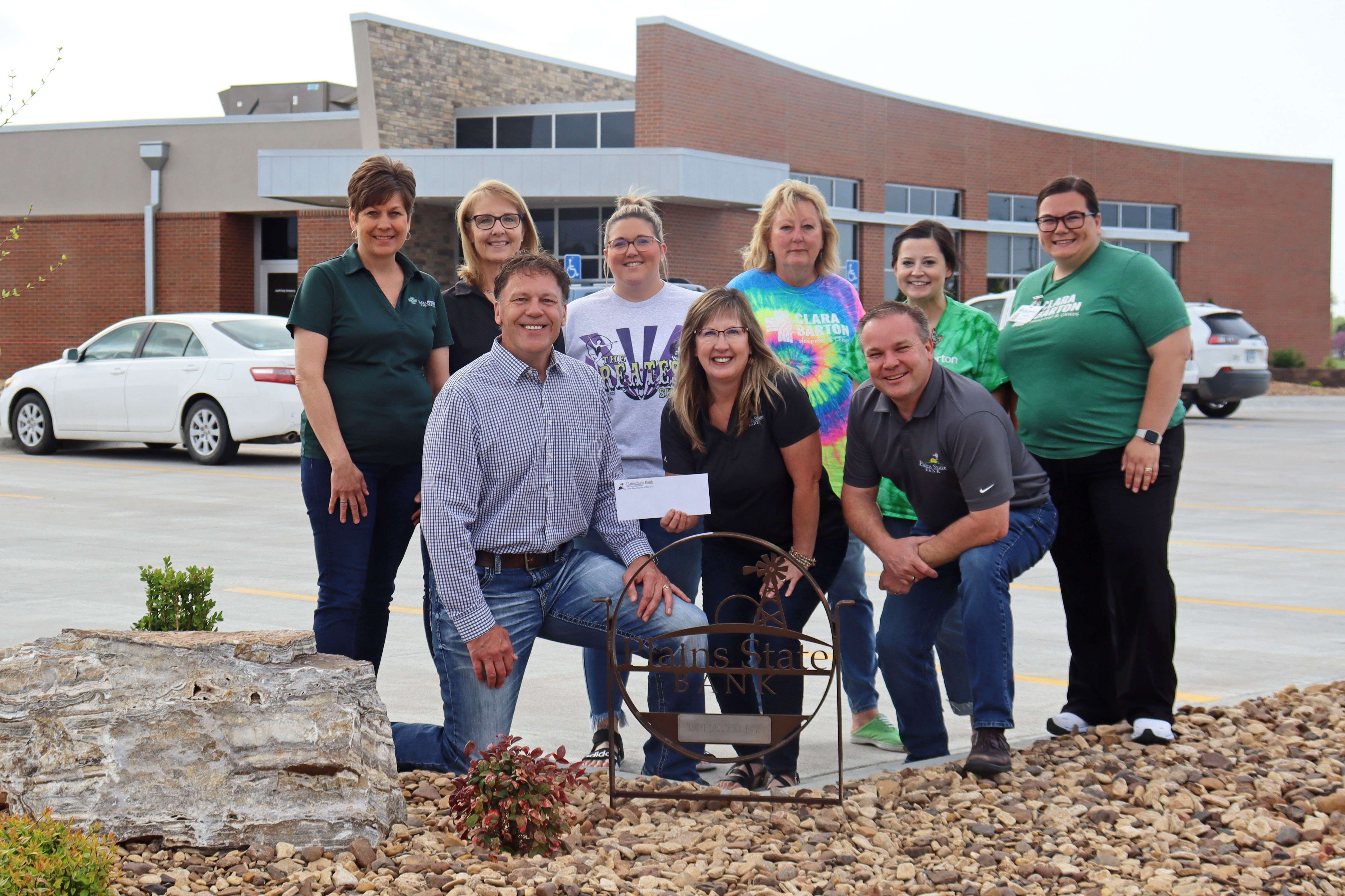 On behalf of Plains State Bank IV, Christy Kuhn, Executive Vice President/COO, and Kelly Higgins, Vice President Branch Manager, present a $15,000 check to Jim Blackwell, President/CEO of Clara Barton Medical Center for the trees and large landscaping island alongside the new walking trail in front of the Great Bend Clinic on McKinley Street. (From left to right - Front Row: Jim Blackwell, Christy Kuhn, Kelly Higgins; Back Row: Michelle Moshier, Karla Crissman, April Gatton, Deb Hawkins, Macy Ingham, Shayla Cook)   