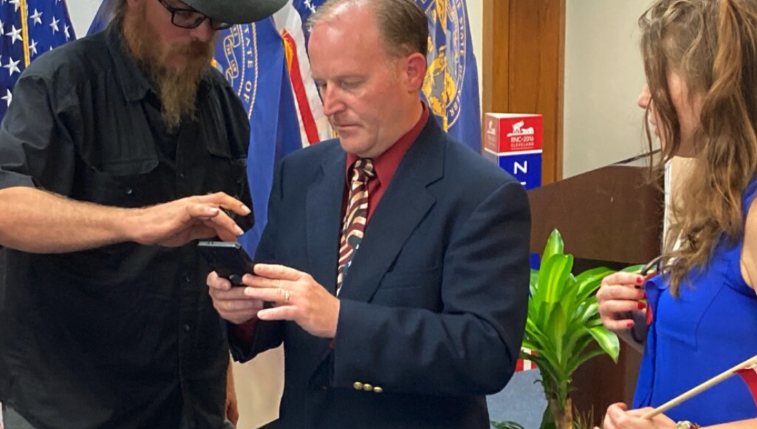 New State GOP Chair Eric Underwood, center, checks a cell phone in July 2022 with others who attended a press conference. (Paul Hammel/Nebraska Examiner)