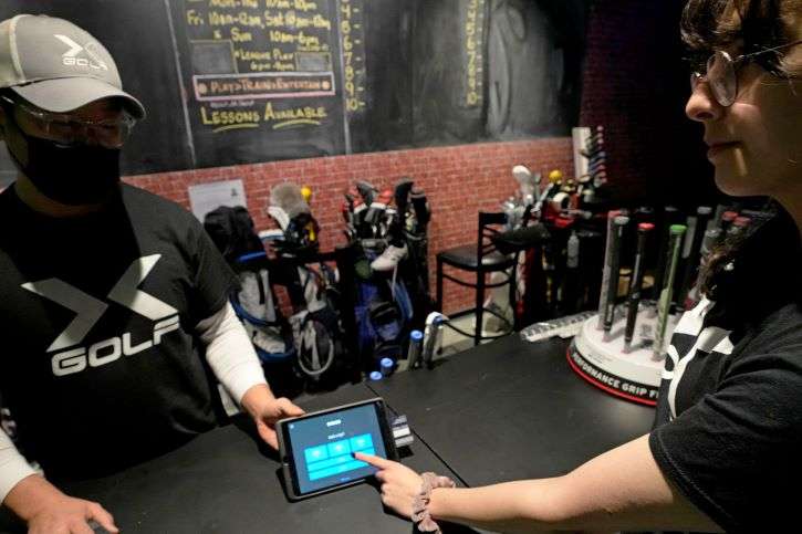 X-Golf manager J.W. Park, left, helps Ashley Moreno to check out at X-Golf indoor golf in Glenview, Ill., Friday, Jan. 20, 2023. Tipping fatigue, it seems, is swarming America as more businesses adopt digital payment methods that automatically prompts customers to leave a gratuity. (AP Photo/Nam Y. Huh)