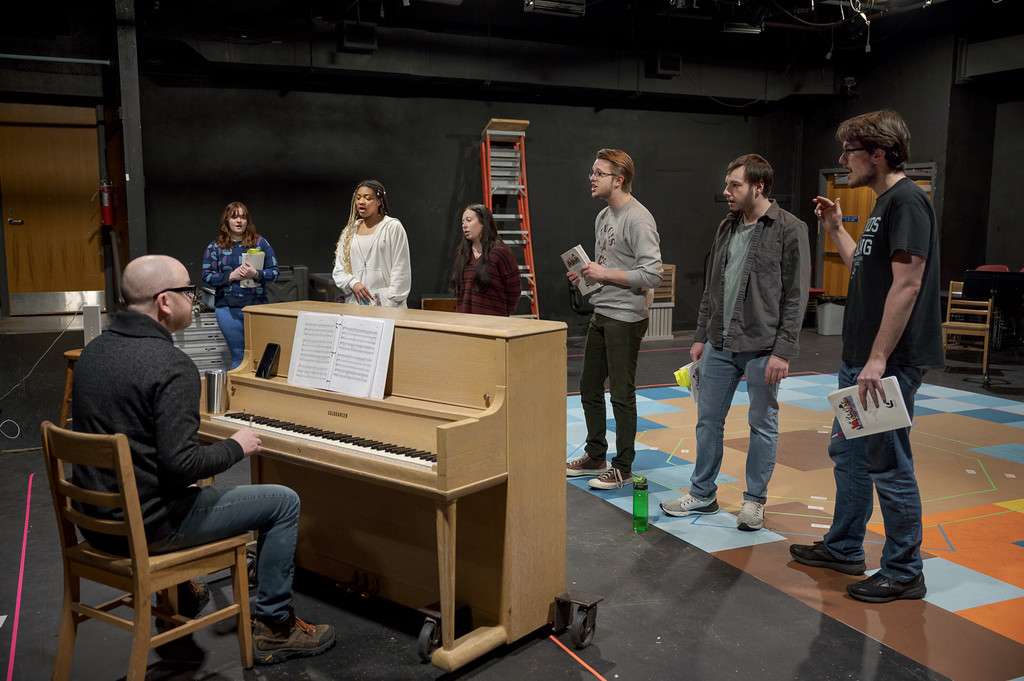 Director Jeremiah Downes, seated, runs a song with cast members, from left, Olivia Freeze, Amber Harvey, Izzy Ashley, Levi O'Dell, Zak Wellnitz, and Jarret Buchholz during a rehearsal for the musical "Working" in January 2023. (Photo by Daniel Binkard/Chadron State College)