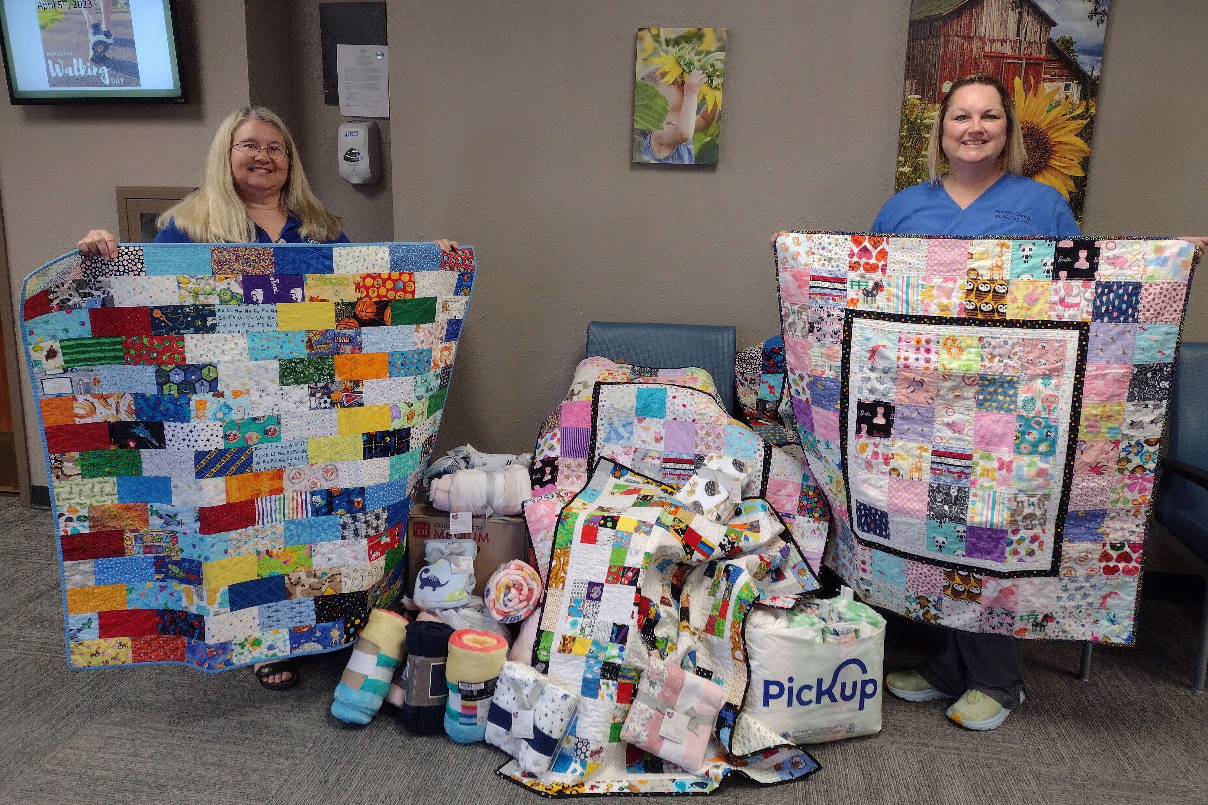 Barton County Health Department Bev Frizell (licensed dietitian) and Debra Higgins (public health nurse) stand, left to right, among the quilts, especially made by a local quilters group for the Rosewood AKTION Club Blanket Drive. The local quilters have contributed to the annual drive for several years now, with all of their homemade quilts being donated to the Health Department.