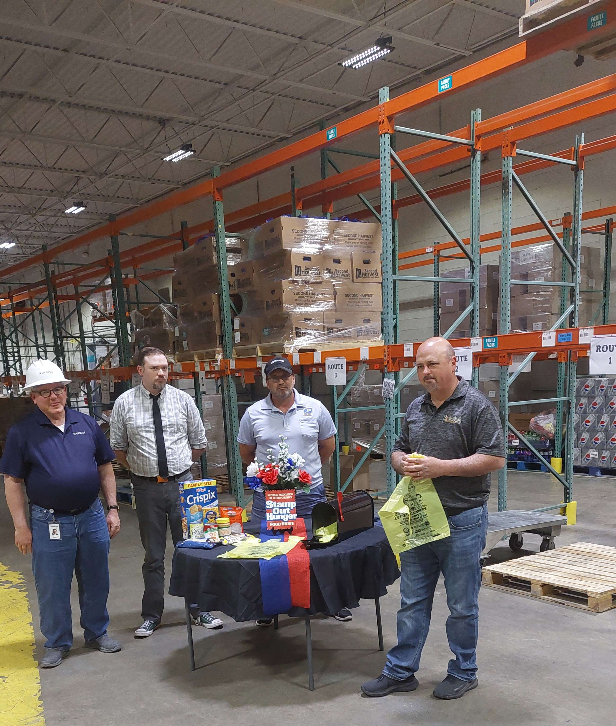 Second Harvest CEO Chad Higdon (right) during the press conference for the Stamp Out Hunger food drive shows off the yellow bags that will be distributed to mail customers on Saturday/ Photo by Matt Pike