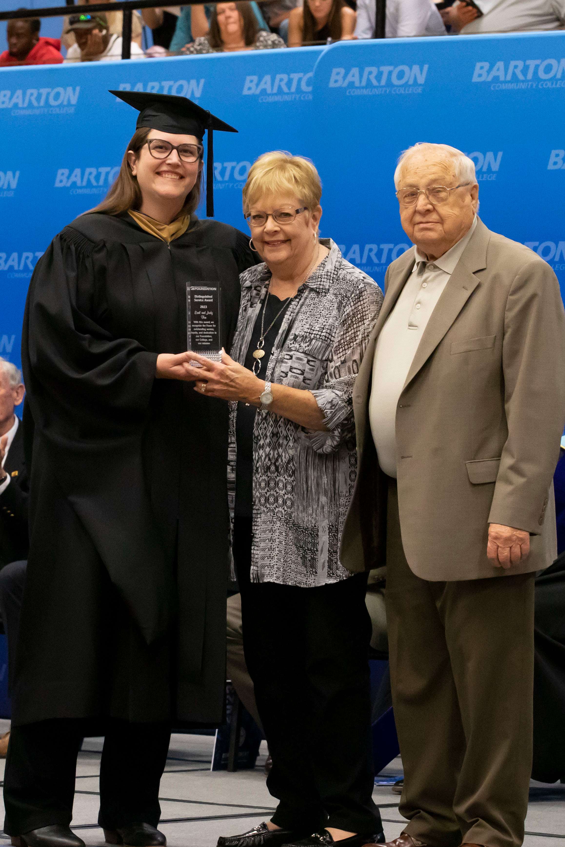 (from left) Barton Executive Director of Institutional Advancement Lindsey Bogner, Distinguished Service Award Recipients Judy and Earl Fox receive their award at the Barton commencement ceremony on Friday, May 12 in the Barton Gymnasium.