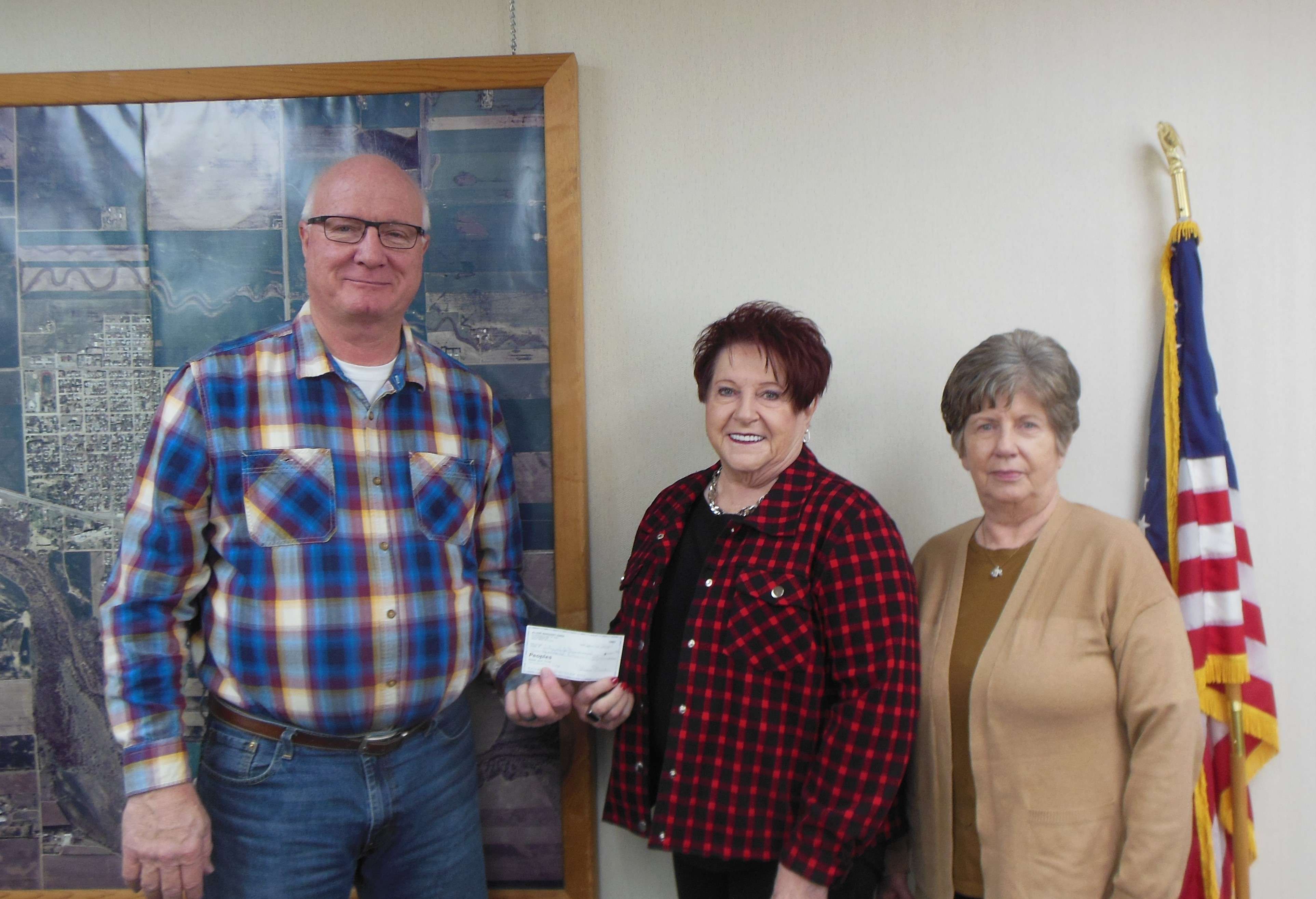 Allene Owen and Marla Isern, representing the Ellinwood High School Class of '68, present Ellinwood City Administrator Chris Komarek with funds for the new billboard project.