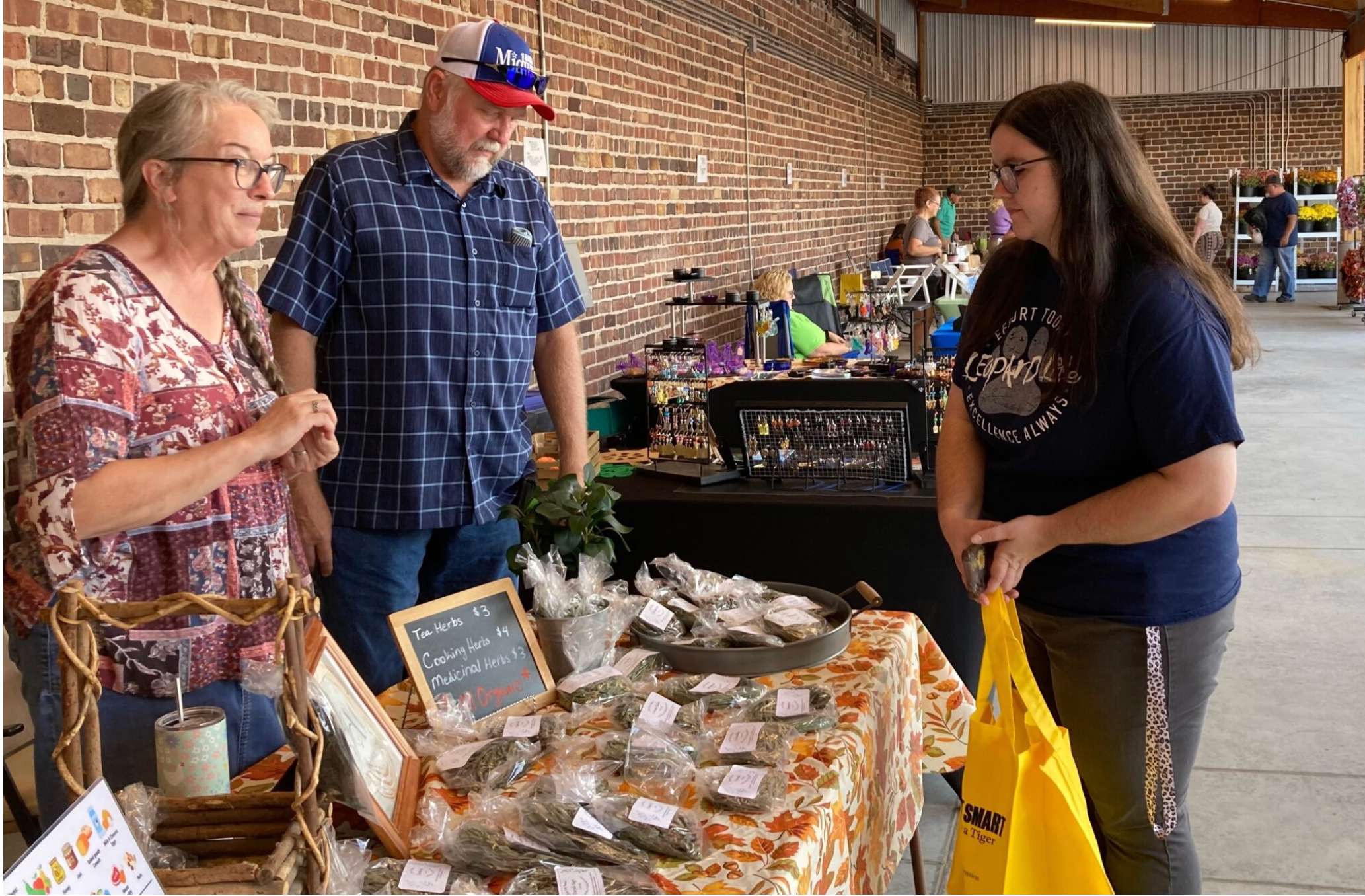  Becky Piquard, left, and her husband, Steve Piquard, of Clark, serve a customer Thursday at their stand for Just Ask Nature at the Randolph County Farmers Market in Moberly. (Steph Quinn/Missouri Independent)