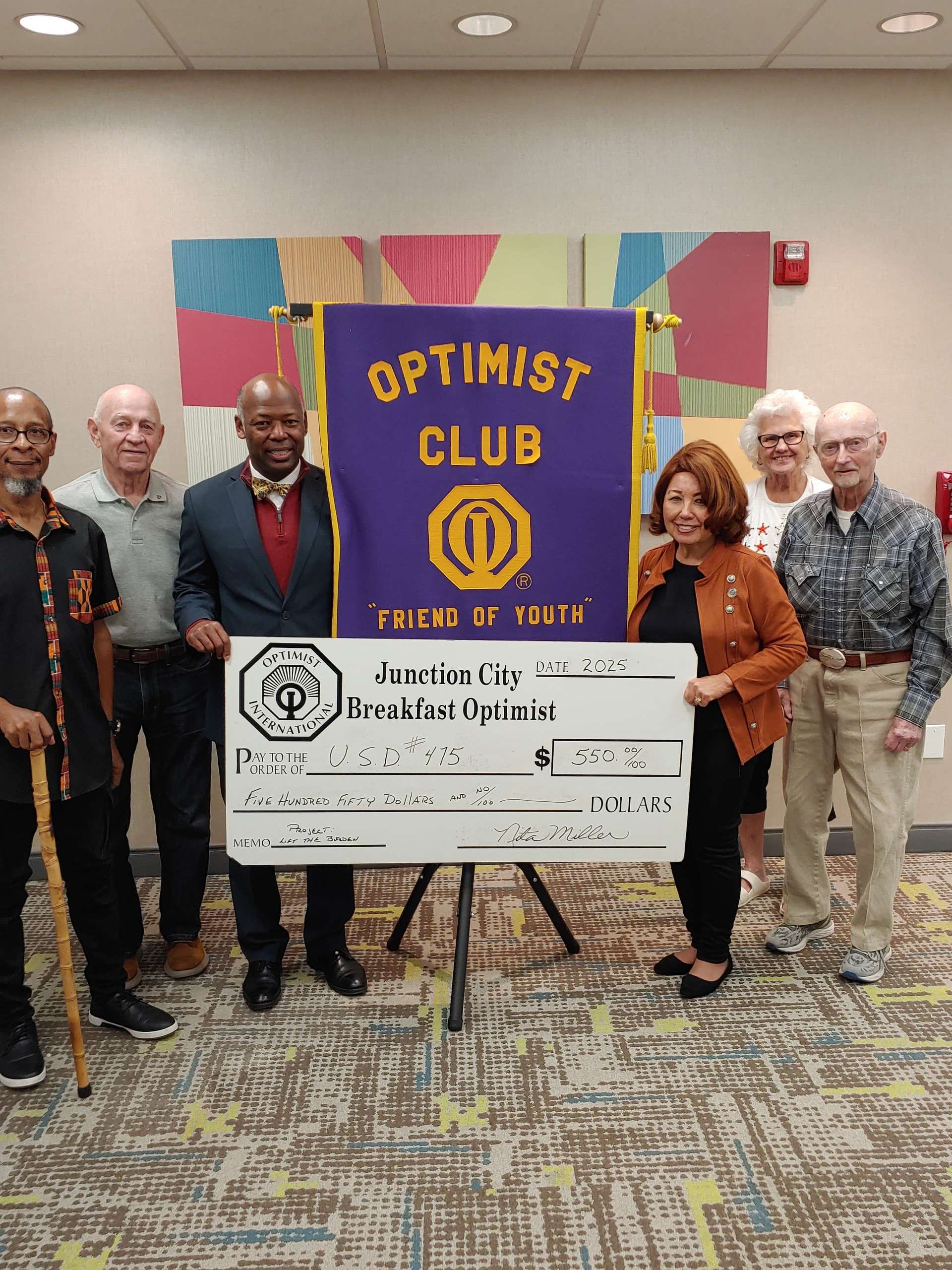 Pictured holding the check are Nita Miller, JC Breakfast Optimist Club President (right holding the check) and Dr. Reginald Eggleston, USD 475 Superintendent (left holding the check). Others pictured are Optimist Club members present at the meeting on October 8. 