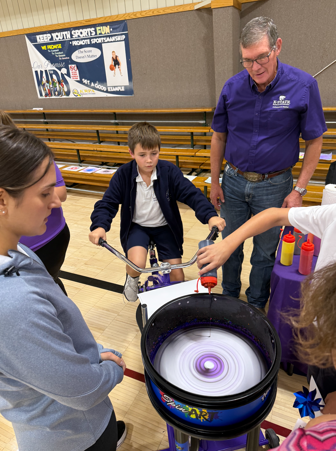 Jay Harris, K-State Extension district director, right, watches as a Holy Family Elementary School student make spin art during Give Fest on Friday. Photo by Cristina Janney/Hays Post