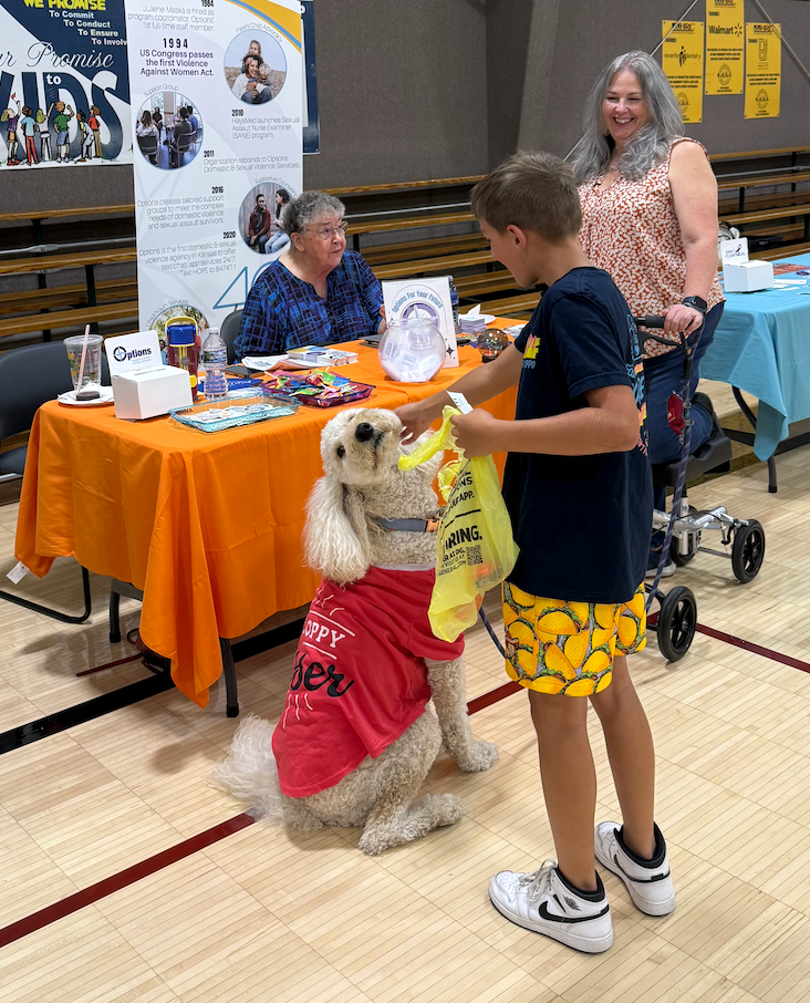 A student pets the Options Domestic and Sexual Violence Services therapy dog, Fonzie, as executive director Jennifer Hecker, right, looks on Friday at Givefest.&nbsp;Photo by Cristina Janney/Hays Post