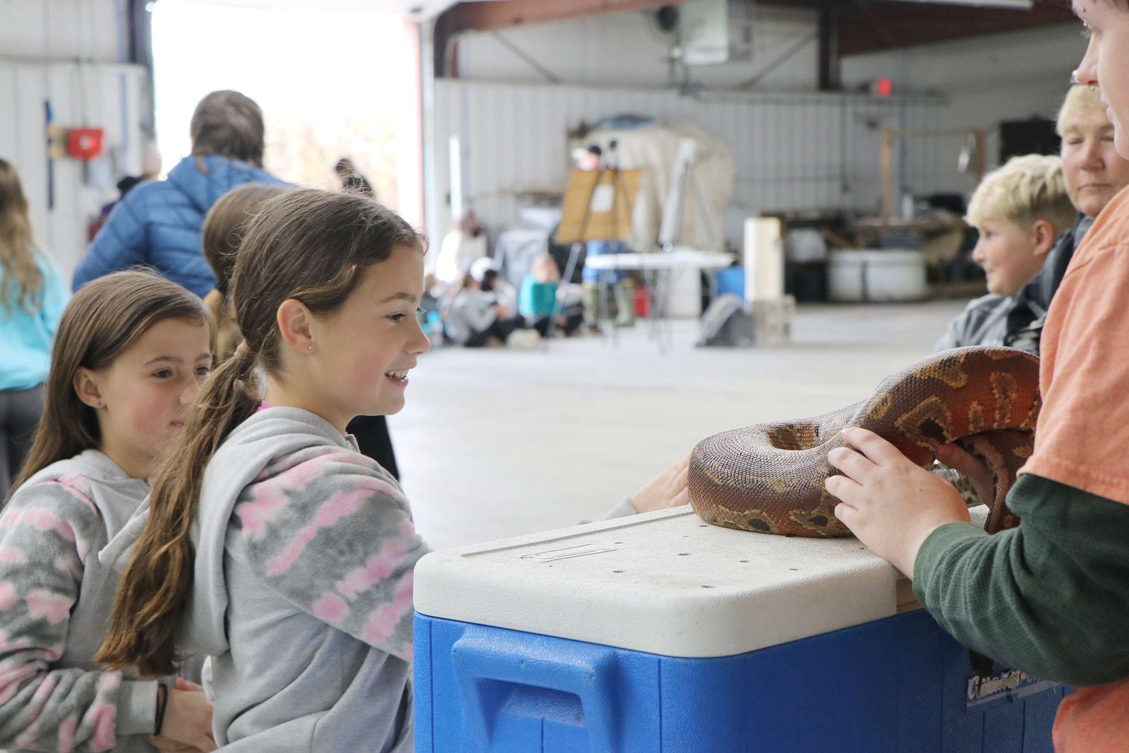 Lake Minatare Elementary students Addison (left) and Allison Engelhaupt line up to ask questions and pet the short-tailed python at the Effects of Water Erosion water station.