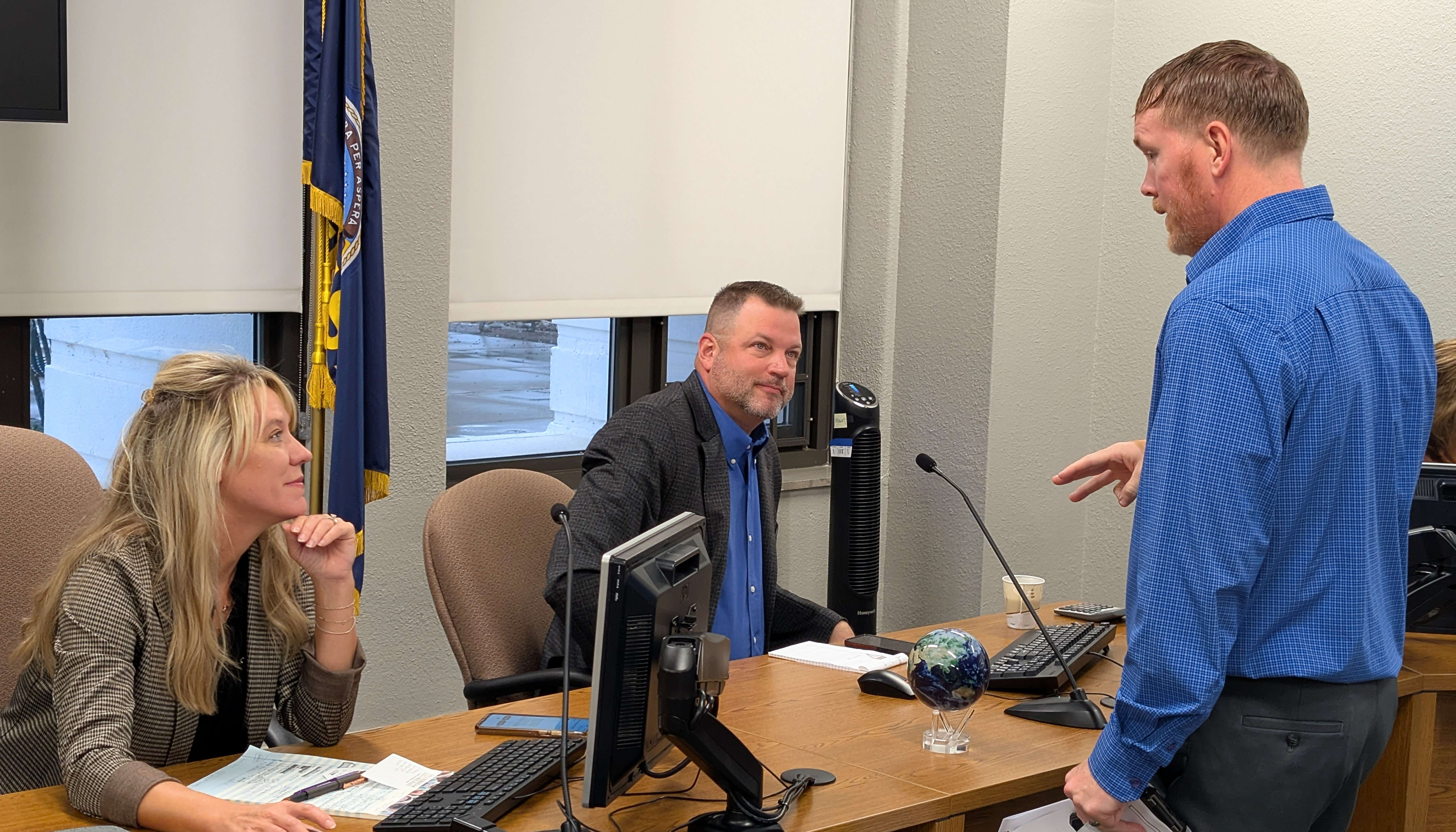 Hoisington City Manager Jonathan Mitchell, standing, visits with Barton County commissioners Tricia Schlessiger and Shawn Hutchinson Tuesday morning after the Commission approved providing economic development funding for a housing project in the community.
