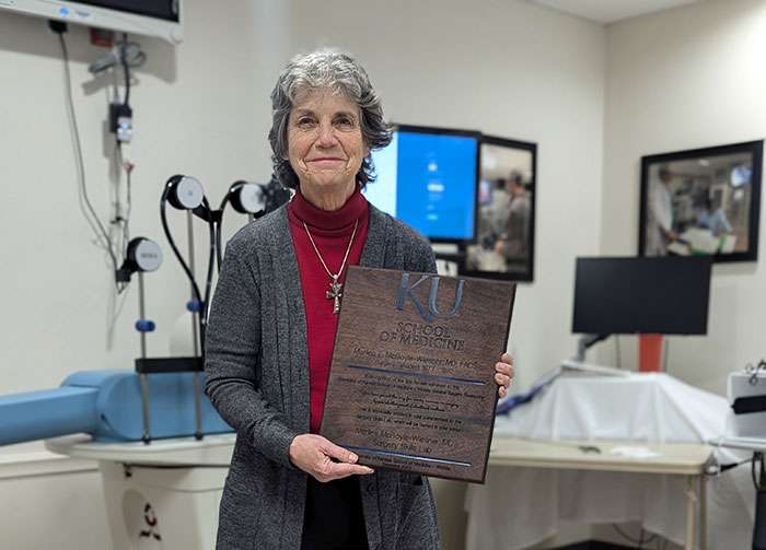 Marilee McBoyle-Wiesner, M.D., holds a plaque in the Surgery Skills Lab named in her honor after her more than 45 years as a surgeon and educator, including professor in the Department of Surgery at KU School of Medicine-Wichita. Courtesy photo