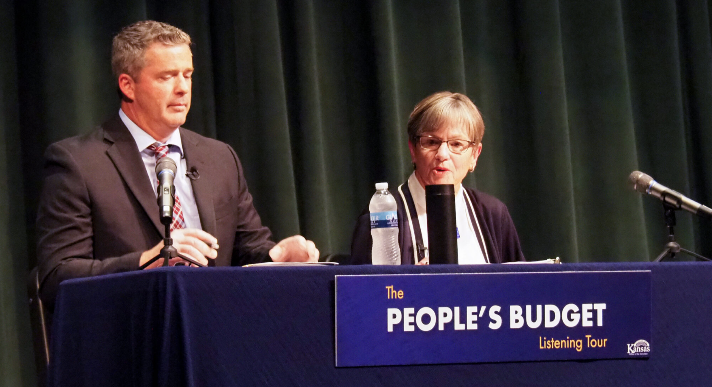 Adam Proffitt, the Kansas state budget director, and Gov. Laura Kelly address a Salina audience at a town hall forum on the state government’s budget. Proffitt is challenging House Speaker Dan Hawkins’ statement that the budget approved by the 2025 Legislature spent $30 million less than was recommended by Kelly. (Tim Carpenter/Kansas Reflector)