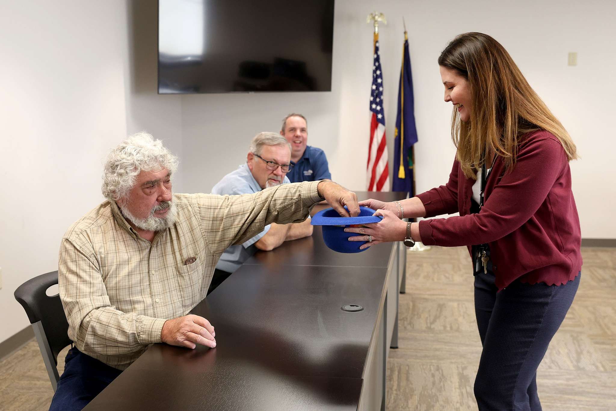 Reno County Commission Chairman Don Bogner reaches in for one of nine names to break the tie for USD 309 Board of Education Position 6 as Reno County Clerk Jenna Fager holds the hat. (Photo courtesy Reno County)