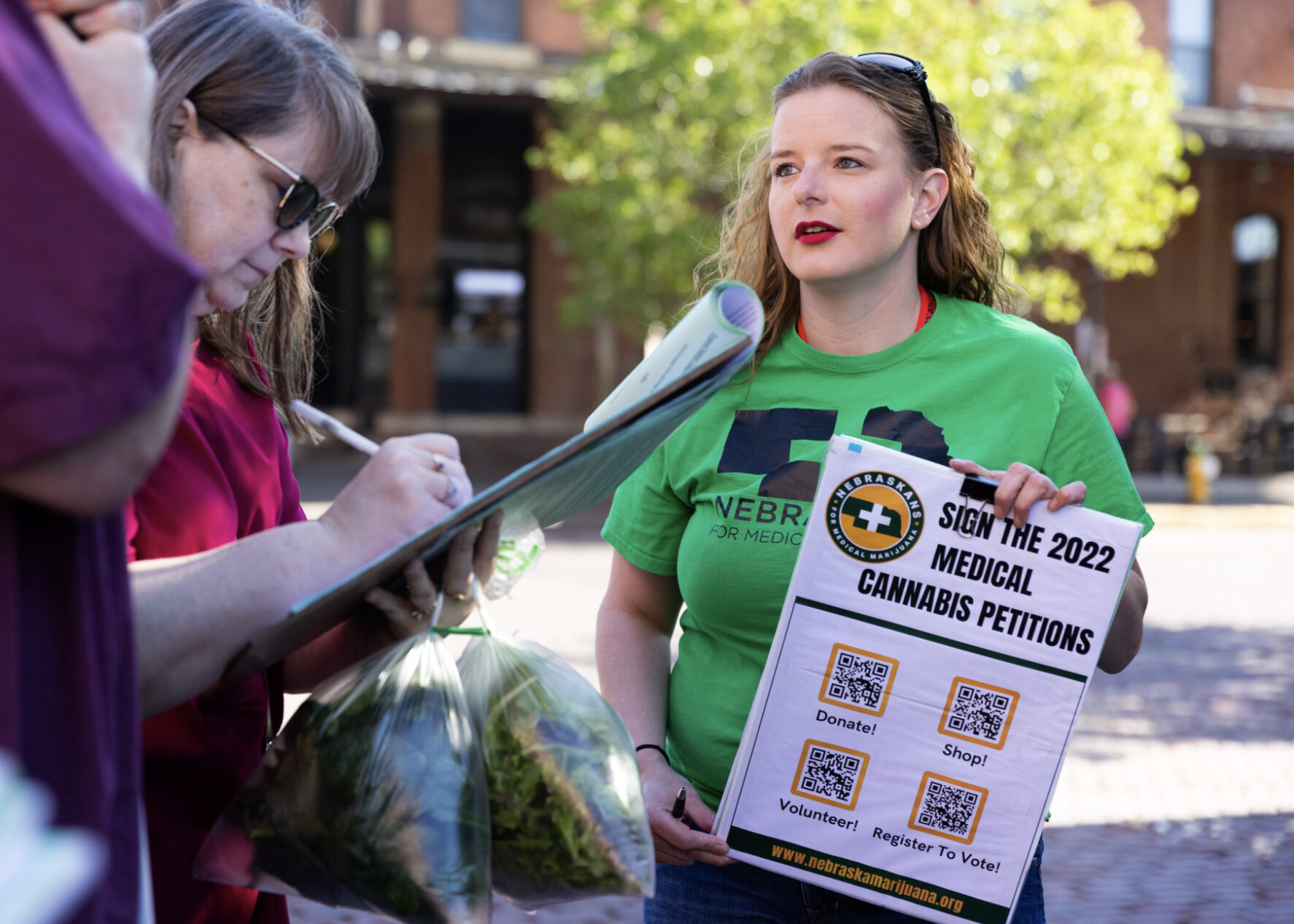 Volunteer Chelle Jones, right, collects signatures from Jeff and Marge Everman of La Vista, left, for a ballot initiative in support of medical cannabis during the Omaha Farmers Market at the Old Market on Saturday, May 14, 2022, in Omaha, Neb. (Rebecca S. Gratz for the Nebraska Examiner)