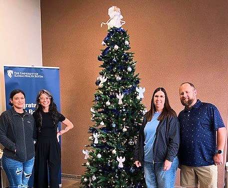 From left: Emma Kelly, Lakin Pafford, Brenda Drake, and Cody Harris encourage the community to support the Sunflower Diversified Services Angel Tree Project. This three in The University of Kansas Health System lobby is one of three options. Kelly, Drake, and Harris represent Sunflower, and Pafford represents the hospital. (photo by Derick Courson)&nbsp;