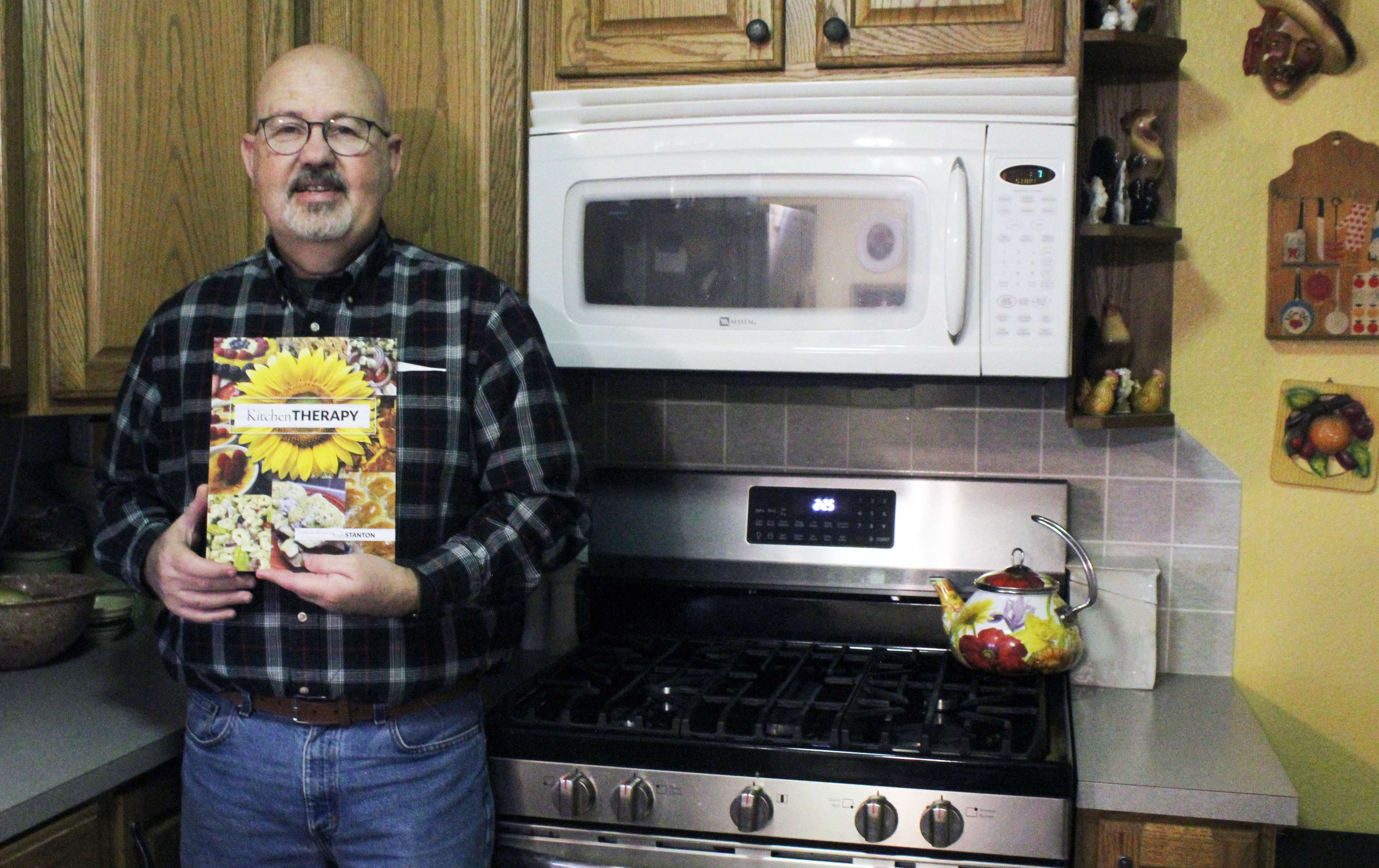 Andy Stanton of Hays displays his new cookbook, "Kitchen Therapy," from his home kitchen in Hays. The cookbook features local favorites like bierocks and green bean dumpling soup and self-taught variations on fancier dishes, such as creme brulee and eggs Benedict. Photo by Cristina Janney/Hays Post