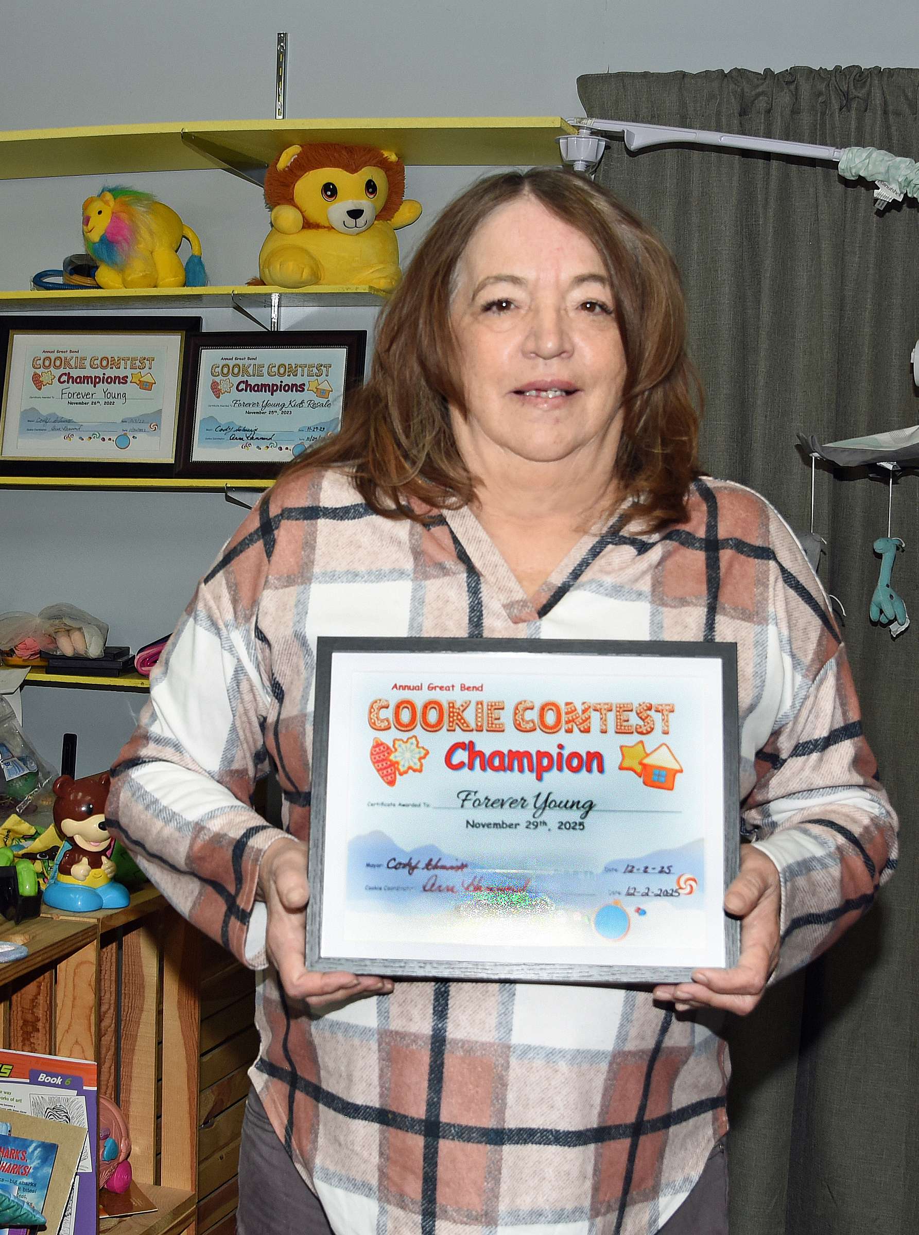 Forever Young (Kids Resale) store owner Betty Hazlett stands with her third framed “Cookie Champion” certificate, along with her two other cookie certificates showcased in the background. A year after finishing out of the top-three, Hazlett regained her championship status this year with her famous Snickerdoodle.