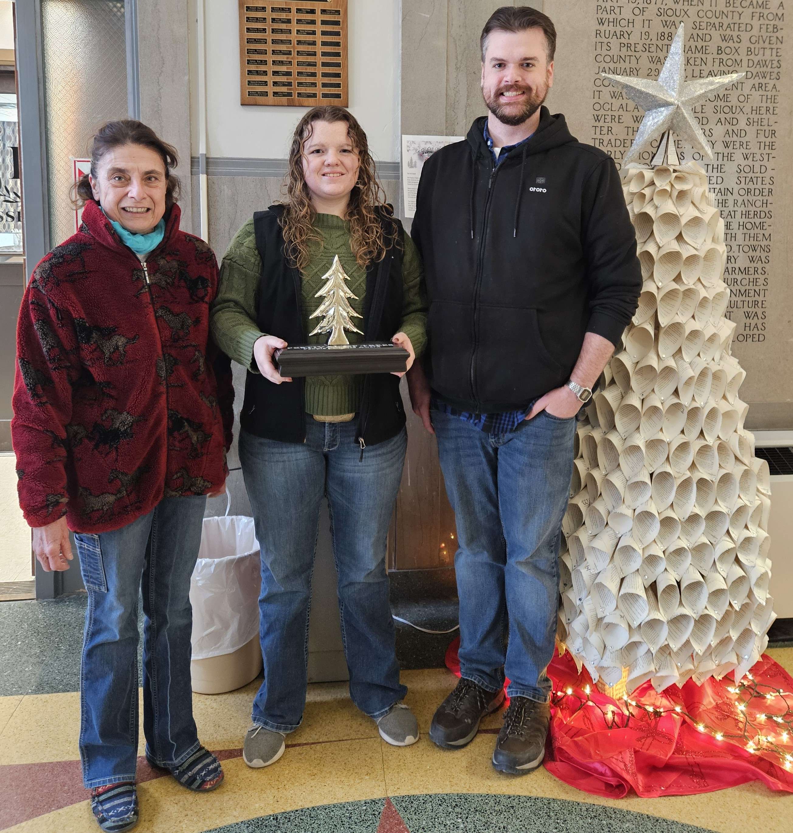 Library staff Rossella Tesch, Renee Redfern and Carl Spicher, from left, accept the People’s Choice traveling trophy for the library’s Out of the Book tree entry at the 2025 Festival of Trees. Photo by Kerri Rempp/Discover Northwest Nebraska