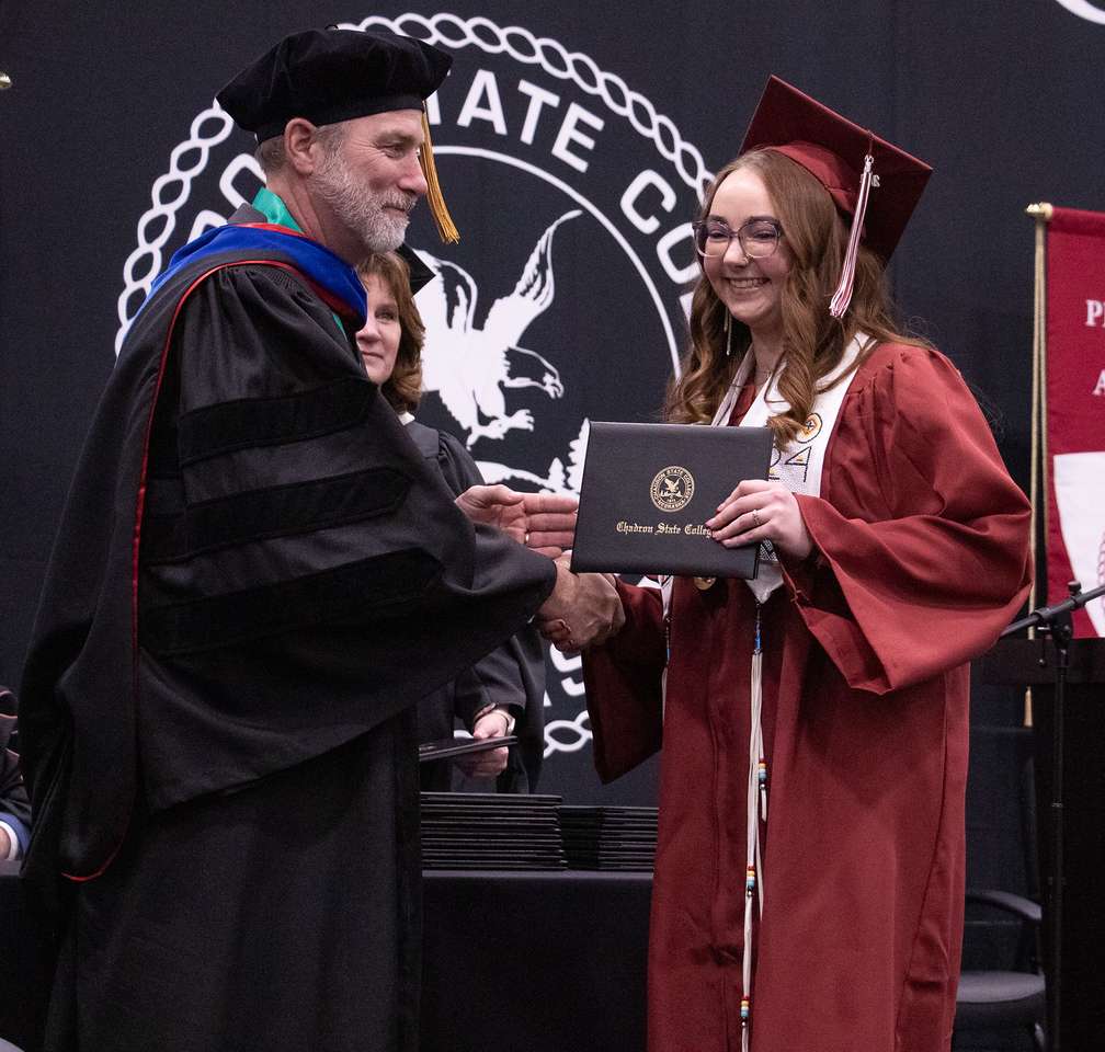 Asia Graham of Newcastle, Wyo., right, receives her diploma from Nebraska State College System Chancellor Paul D. Turman, left, during Chadron State College's Winter Commencement in the Chicoine Center on Dec. 13, 2024. (Photo by Tena L. Cook/Chadron State College)
