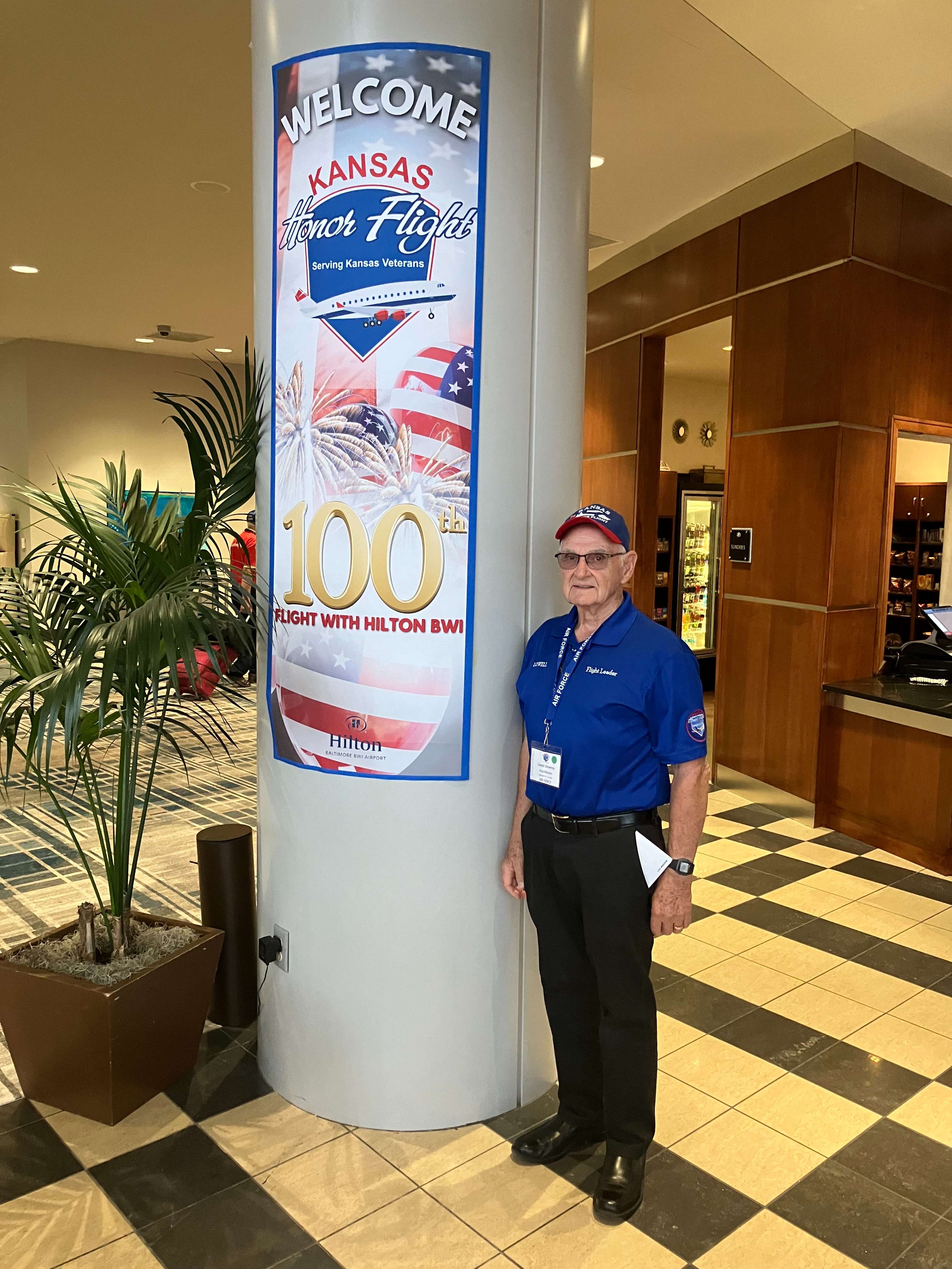 Lowell Downey stands next to a sign celebrating the 100th Kansas Honor Flight at the Hilton Baltimore BWI Airport. Downey participated in the milestone trip honoring Kansas veterans. (Courtesy Photo)