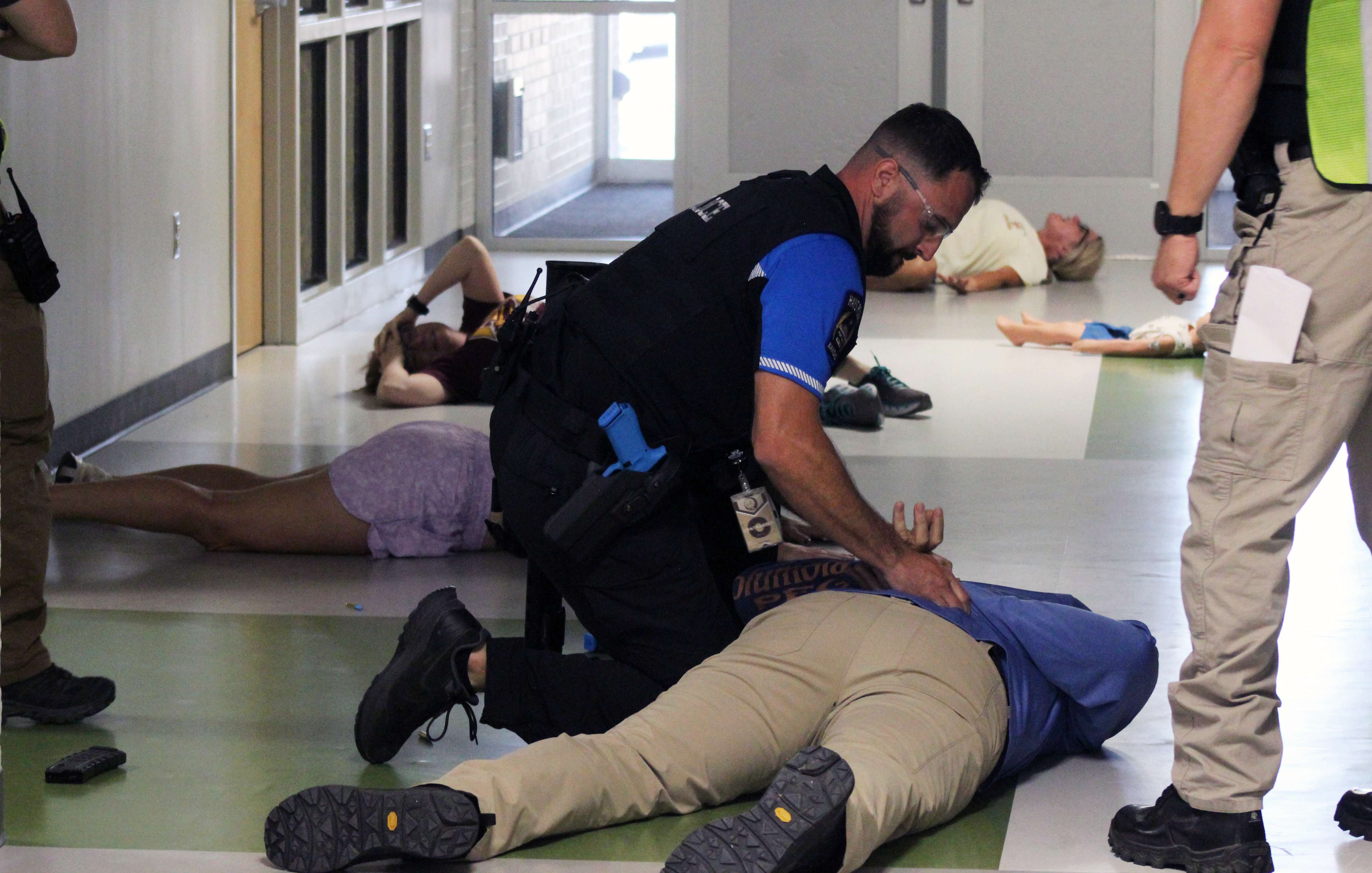 A Hays police officer handcuffs a perpetrator as a training officer looks on during an active shooter drill Wednesday at Roosevelt Elementary School. Actors portray injured victims in the background. Photo by Cristina Janney/Hays Post