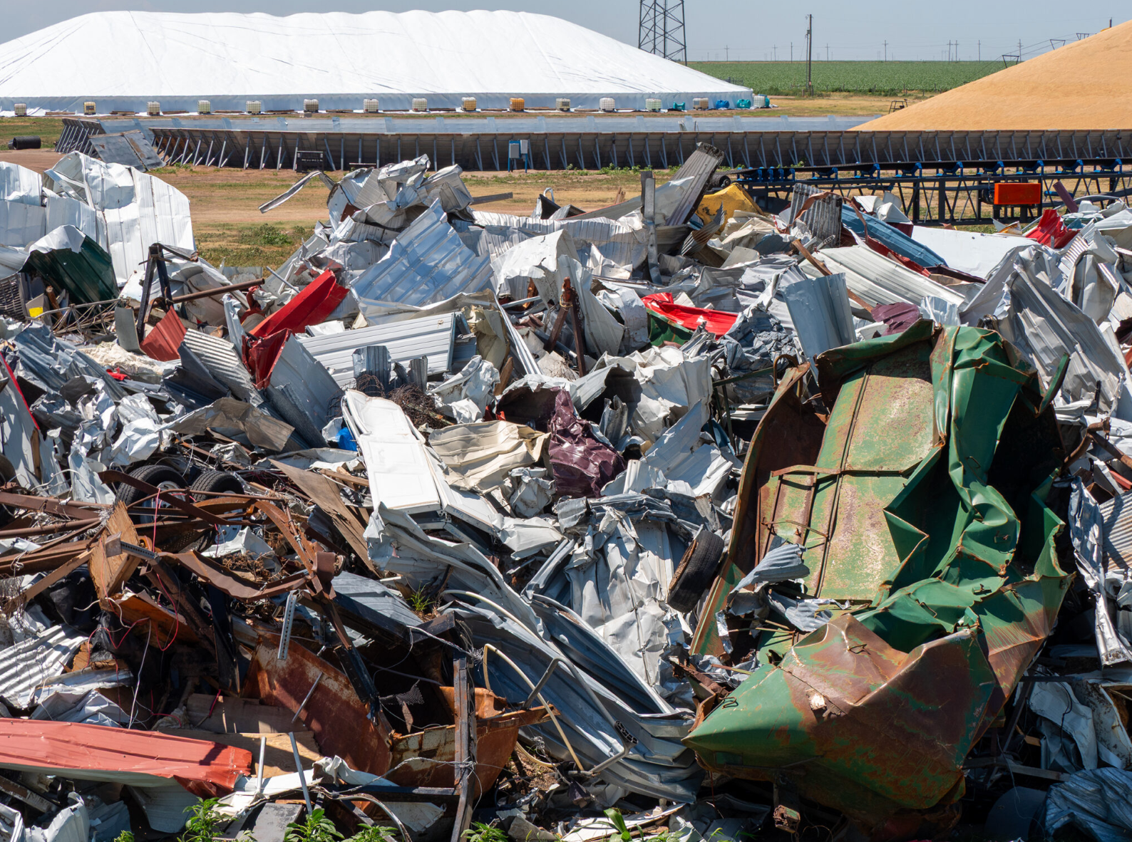 Rubble from the May tornado could still be seen on July 9, 2025, in Grinnell. The town has continued cleaning up and making repairs but it will take months to recover. Under tarps in the background, Frontier Ag is storing grain after after its Grinnell facility sustained $5.5 million in damage. (Sherman Smith/Kansas Reflector)
