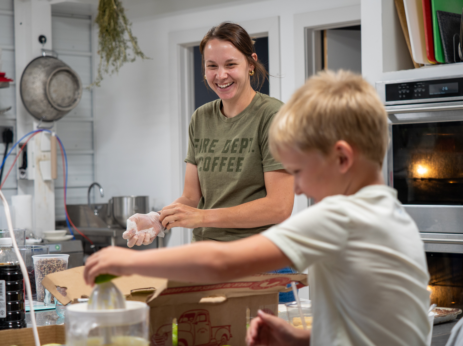 Tristan Bixenman, owner of Meraki Market coffee shop and bakery in Grainfield, is helped by her son, Kip, in the kitchen. Bixenman provided food for volunteers and also worked for hours at the VFW in Grinnell after the tornado hit the town in May. (Sherman Smith/Kansas Reflector)