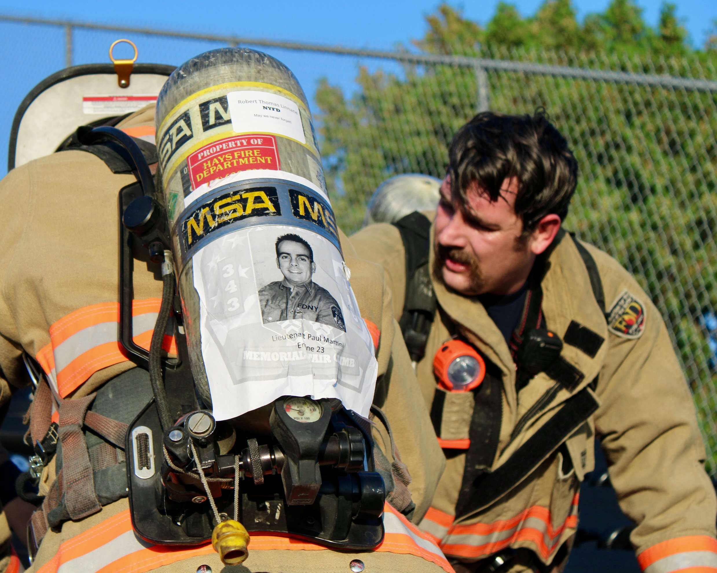 Firefighters resting at the 9/11 Memorial Stair Climb. A picture of fallen New York Fire Department Lieutenant Paul Martini is taped to the back of a firefighter's gear. Photo by Tony Guerrero/Hays Post