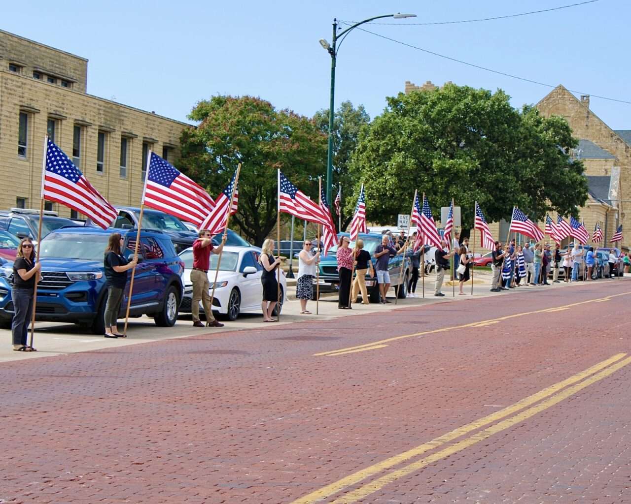 Hays residents with American flags lined up on 13th Street in Hays. Photo by Tony Guerrero/Hays Post