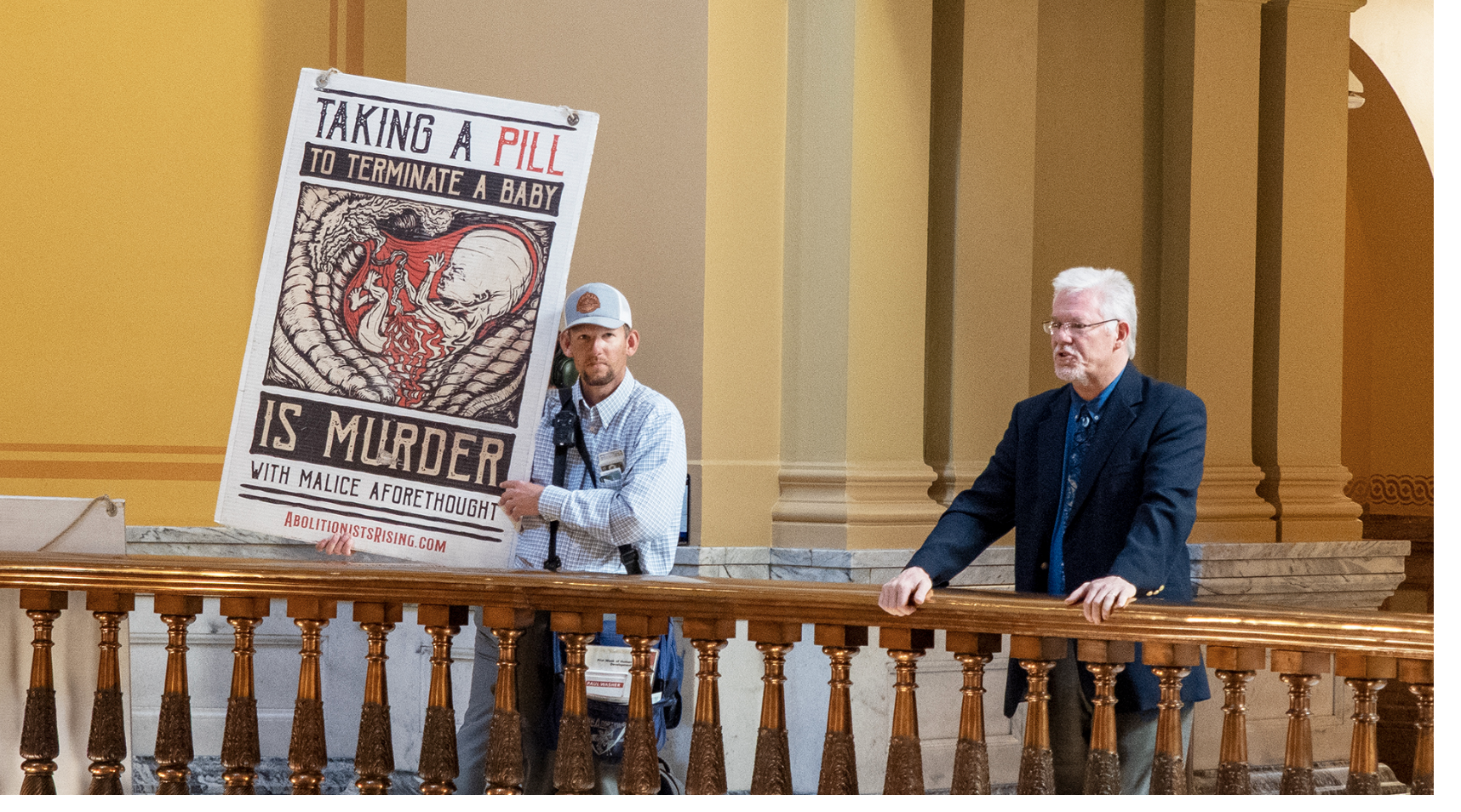 Nicholas Heald, of Wichita, holds a sign demonstrating his anti-abortion views on April 10, 2025, at the third floor center railing between the House and Senate. (Sherman Smith/Kansas Reflector)