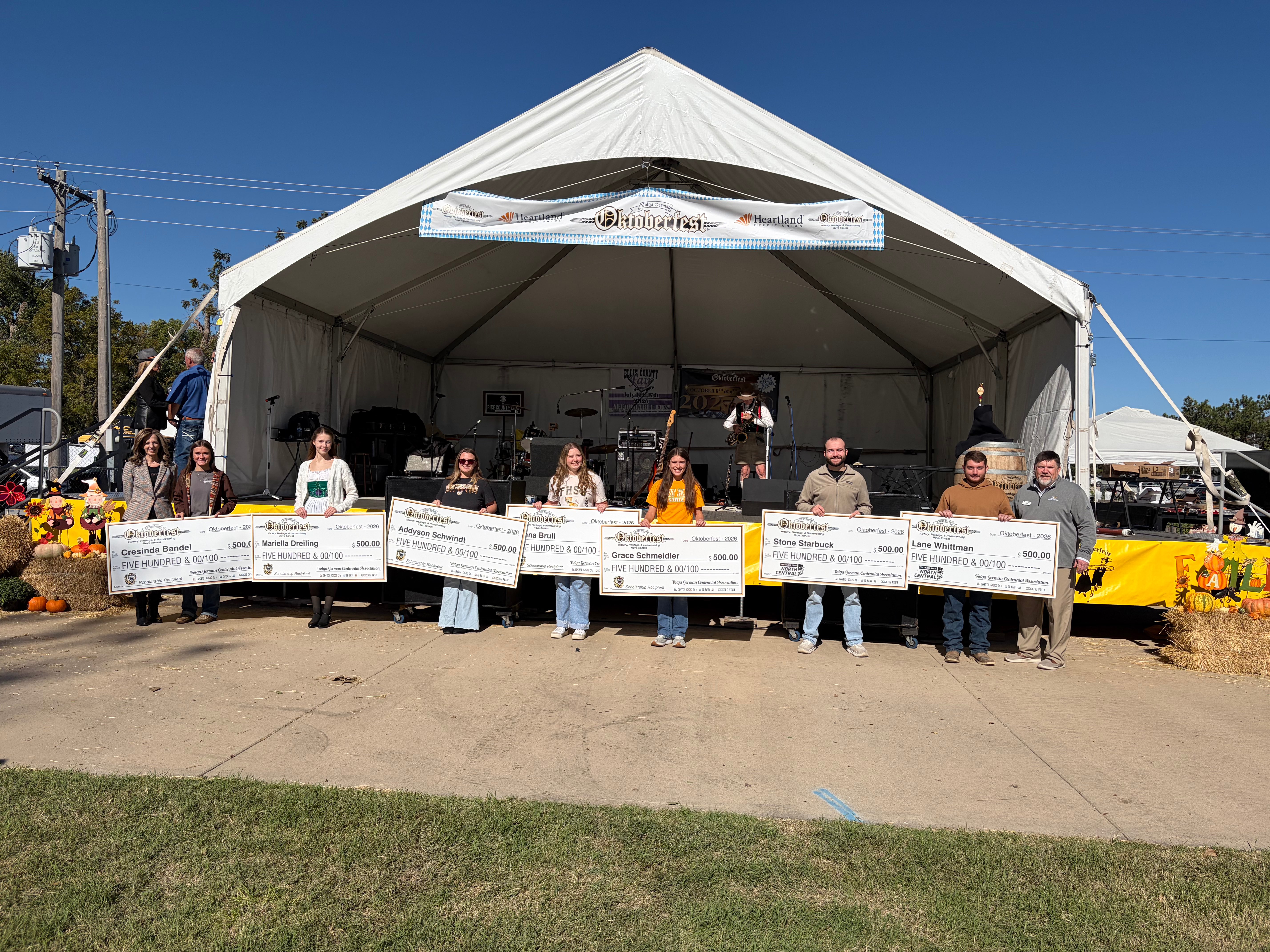 Students stand next to FHSU President Tisa Mason and Eric Burks, president of Fort Hays Tech North Central as they receive $500 scholarships from FHSU in the at Oktoberfest Hays 2026. From left: FHSU President Tisa Mason, Cresinda Bandel, Mariella Dreilling, Addyson Schwindt, Jenna Brull, Grace Schmeidler, Stone Starbuck, Lane Whittman, and Eric Burks.&nbsp;Photo by Alin Hett/Hays Post.&nbsp;
