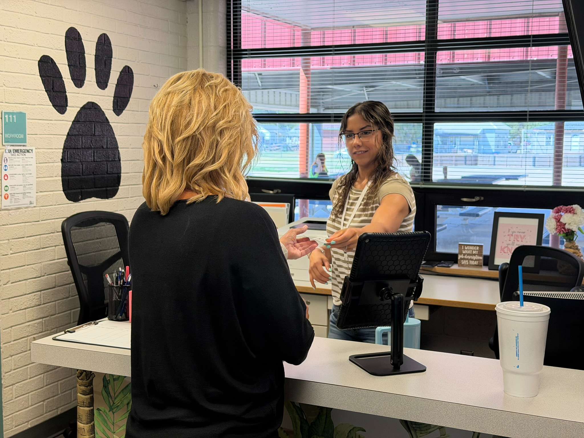 Park Elementary Secretary Ingry Martinez hands Board of Education Member Karen Lindberg her visitor badge after completing the new Raptor VisitorSafe check-in process at the front desk.