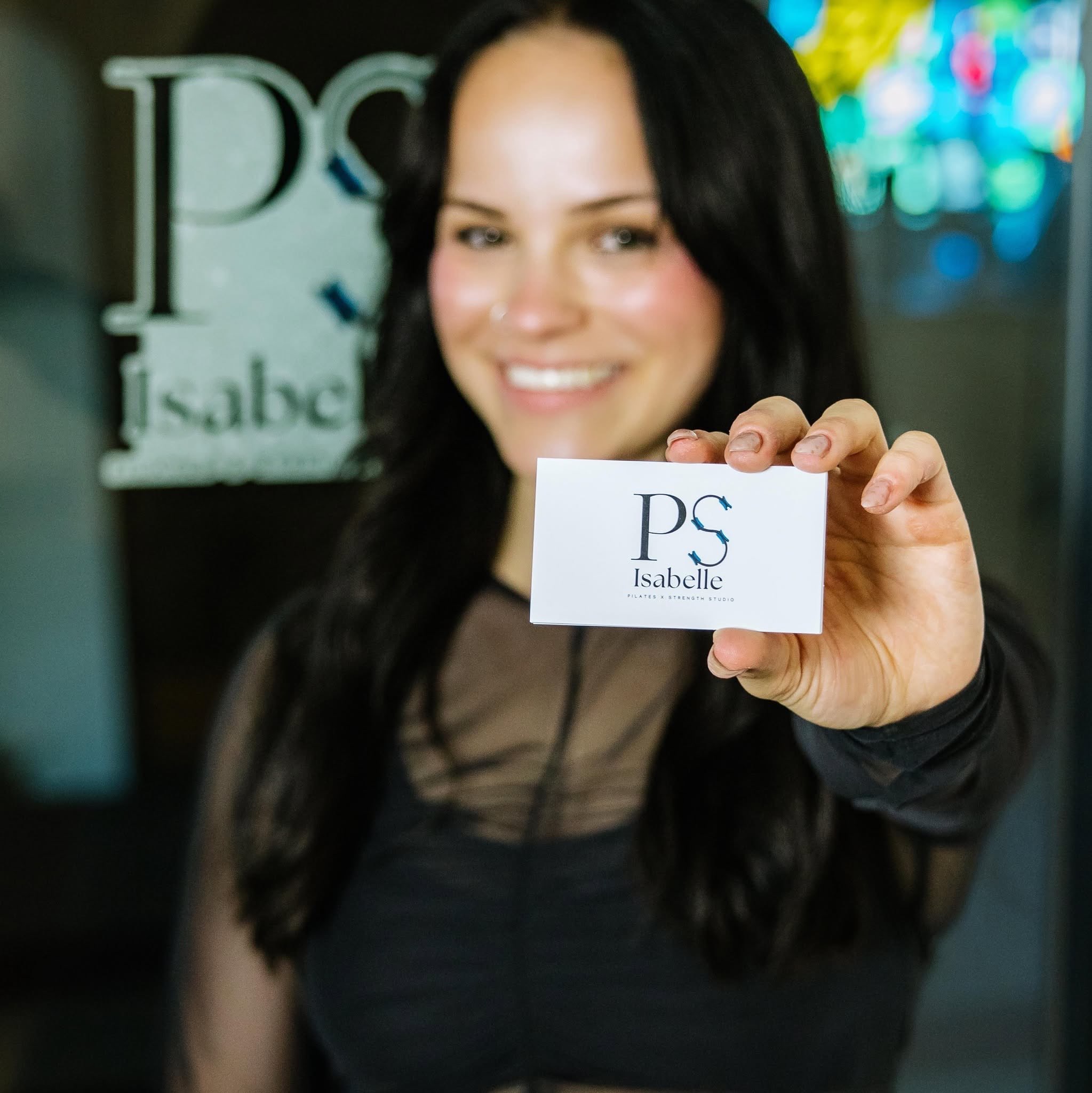 Isabelle Braun, owner of &nbsp;Pilates &amp; Strength Studio by Isabelle, also known as P.S. Isabelle, holding her business card while standing in front of her business. Courtesy photo from Facebook.&nbsp;