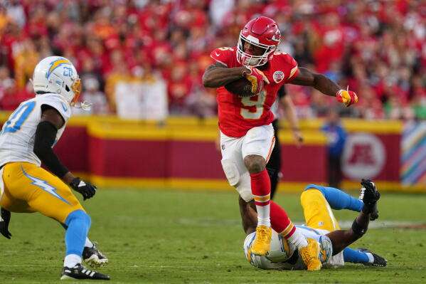 Kansas City Chiefs running back Kenneth Walker III (9) escapes a tackle attempt by Los Angeles Chargers linebacker Del'shawn Phillips, bottom, as Cam Hart (20) moves in to make this stop during the second half of an NFL football game in Kansas City, Mo., Sunday, Oct. 18, 2026. (AP Photo/Ed Zurga)