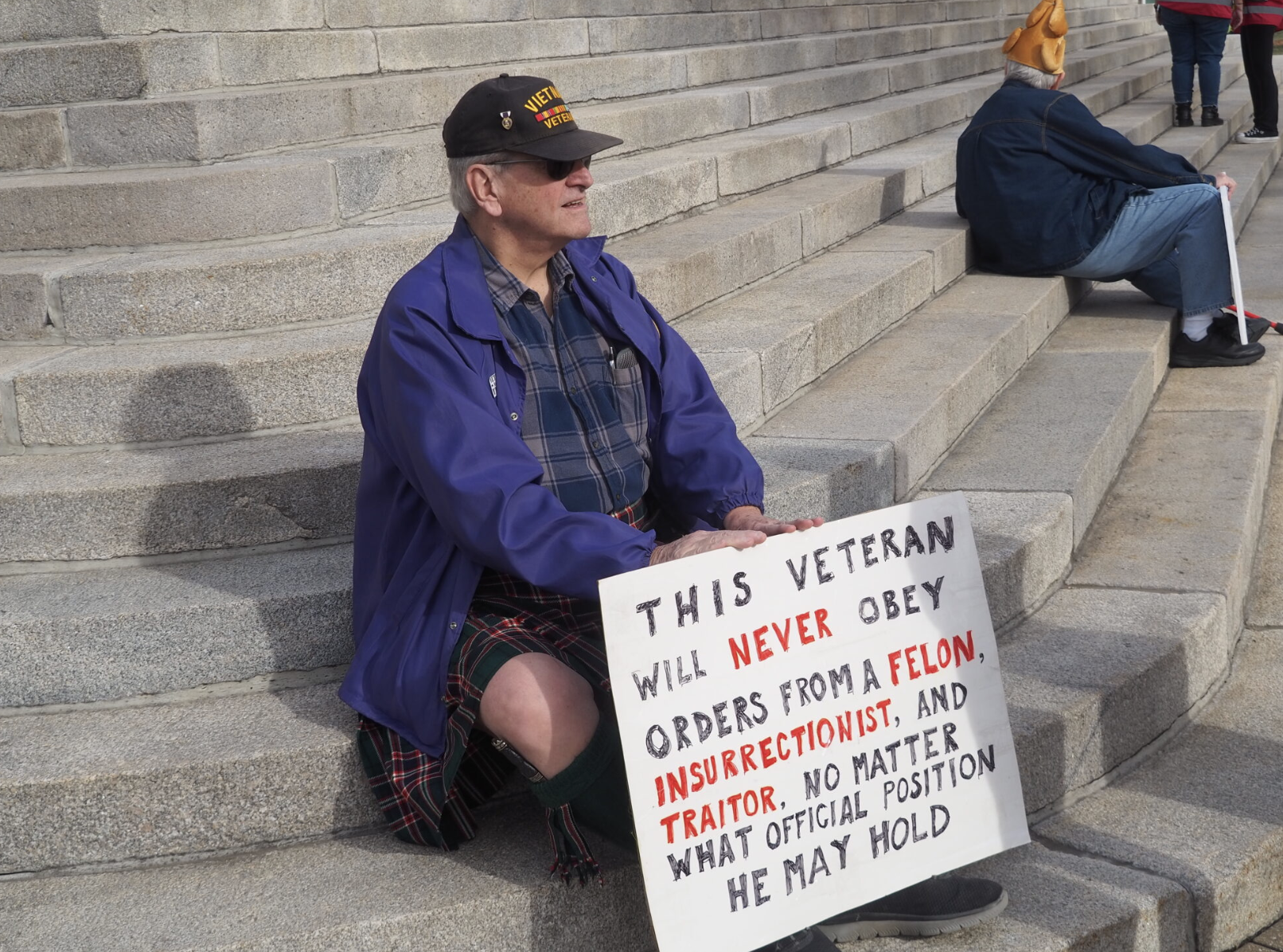 Doug McGaw, of Emporia, sits during a Feb. 16, 2026, protest outside the Capitol. The Vietnam veteran says he won’t follow orders of a felon, insurrectionist or traitor regardless of the individual’s official position. (Photo by Tim Carpenter/Kansas Reflector)