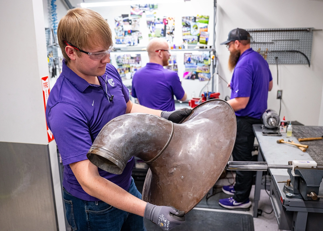 Chase Wassom rolls out the dents on the bell of the horn he is restoring. The steel tool requires finesse — a ball bearing rolls around and helps shape and knead out dents in an instrument's metal.&nbsp;Photos by Jeff Moore/Kansas State University